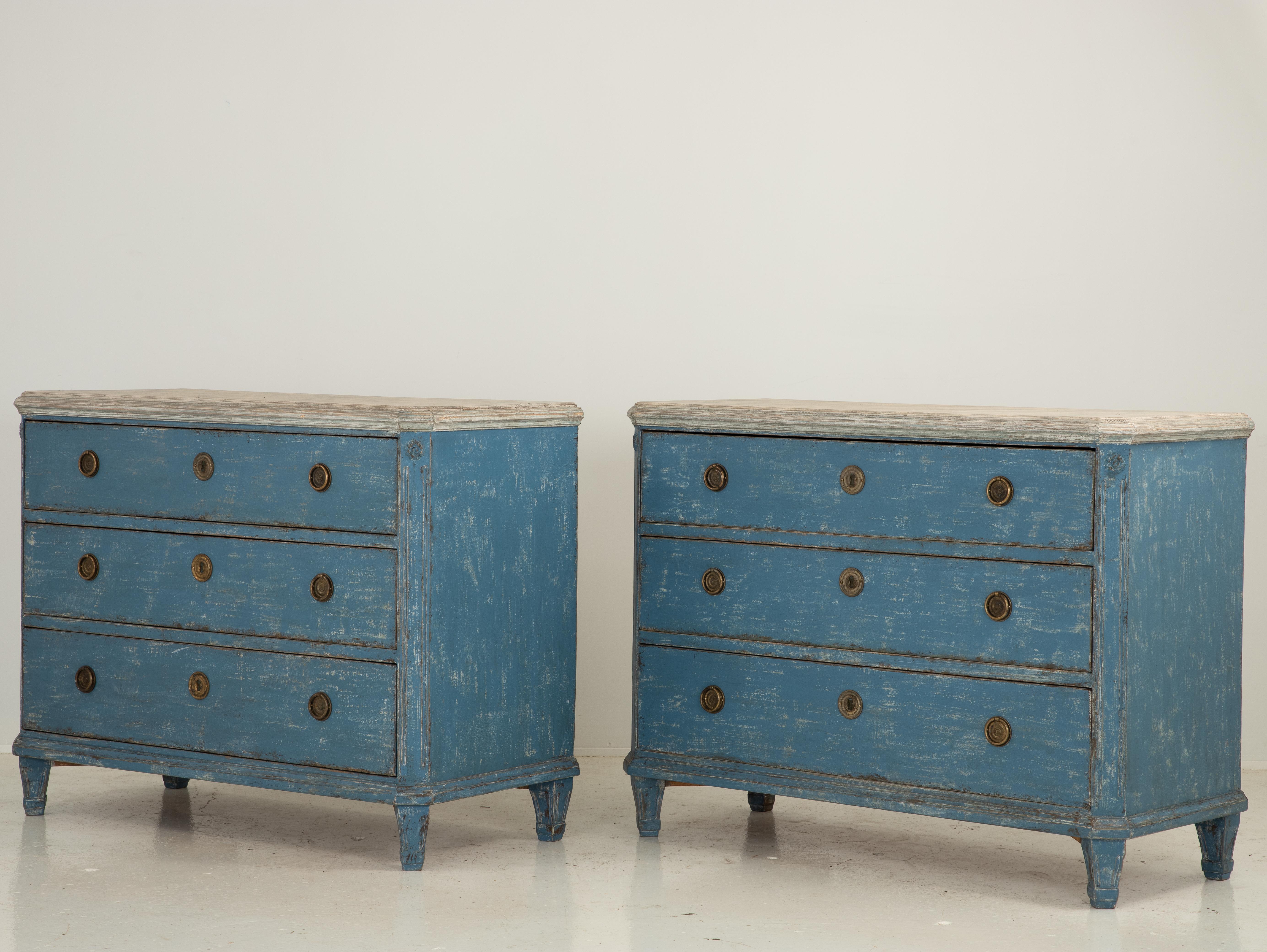 A late 19th or early 20th century pair of painted Gustavian style commodes. Each commode has three drawers with brass ring pulls. Canted corner with a rosette motif and a fuax marble finish top sets this off as distinctly Gustavian in style.