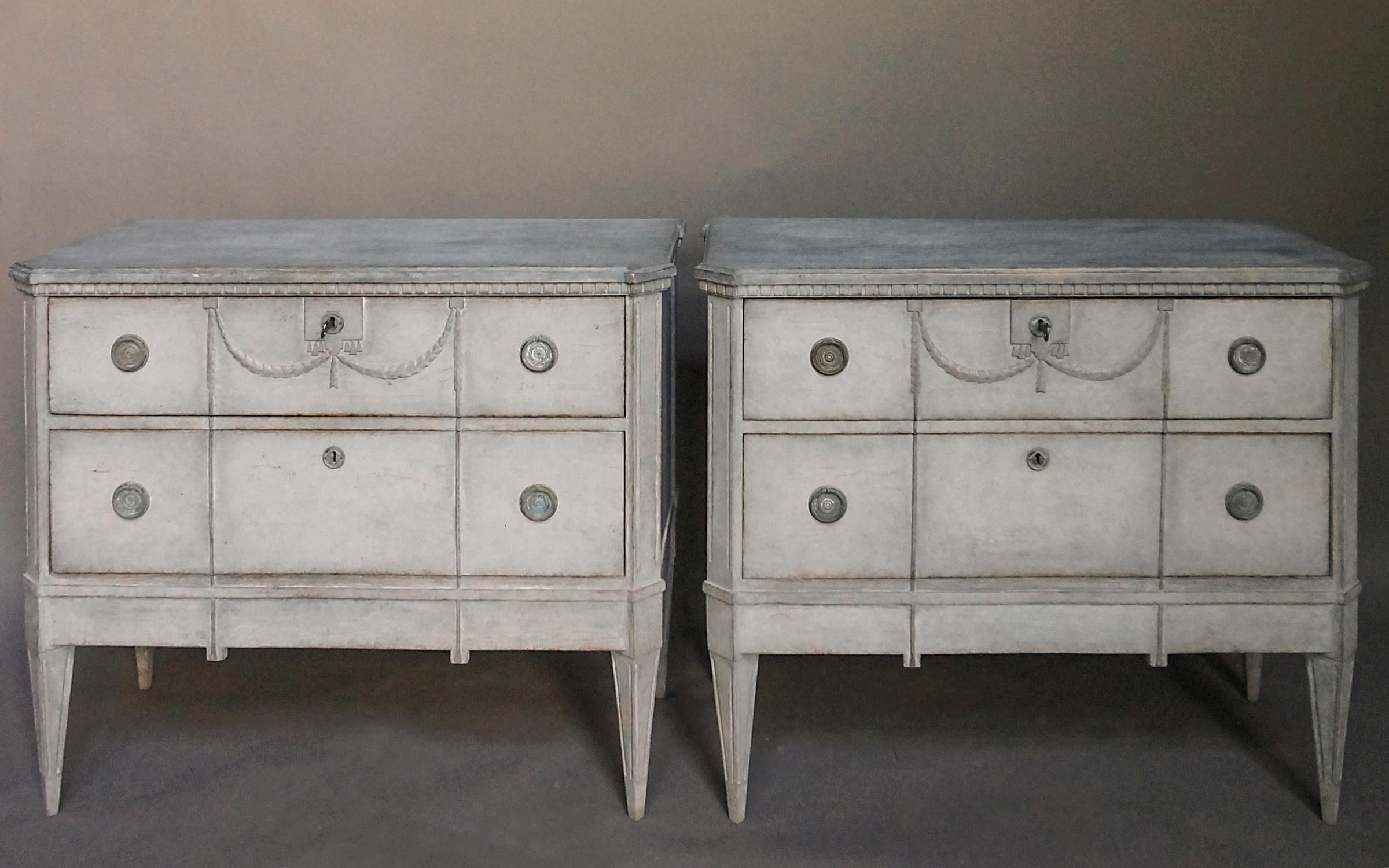 Pair of two-drawer commodes in the Gustavian style, Sweden, circa 1870 with applied swags and tassels. Dentil molding under the shaped top, canted corners and tapering square legs.