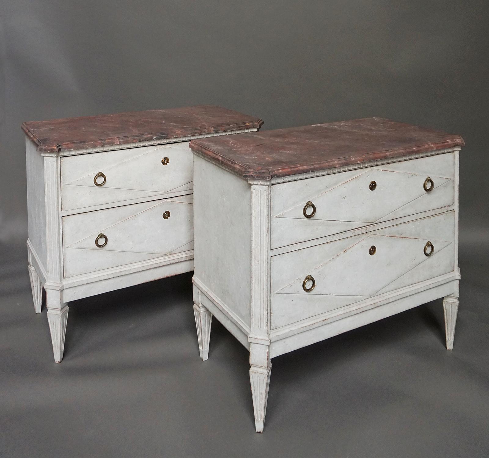 Pair of two drawer chests, Sweden circa 1870, in the Gustavian style. Shaped tops painted as red marble have dentil molding below. Each drawer front has a raised lozenge and brass pulls. Fluted corner posts extend to tapering square feet.