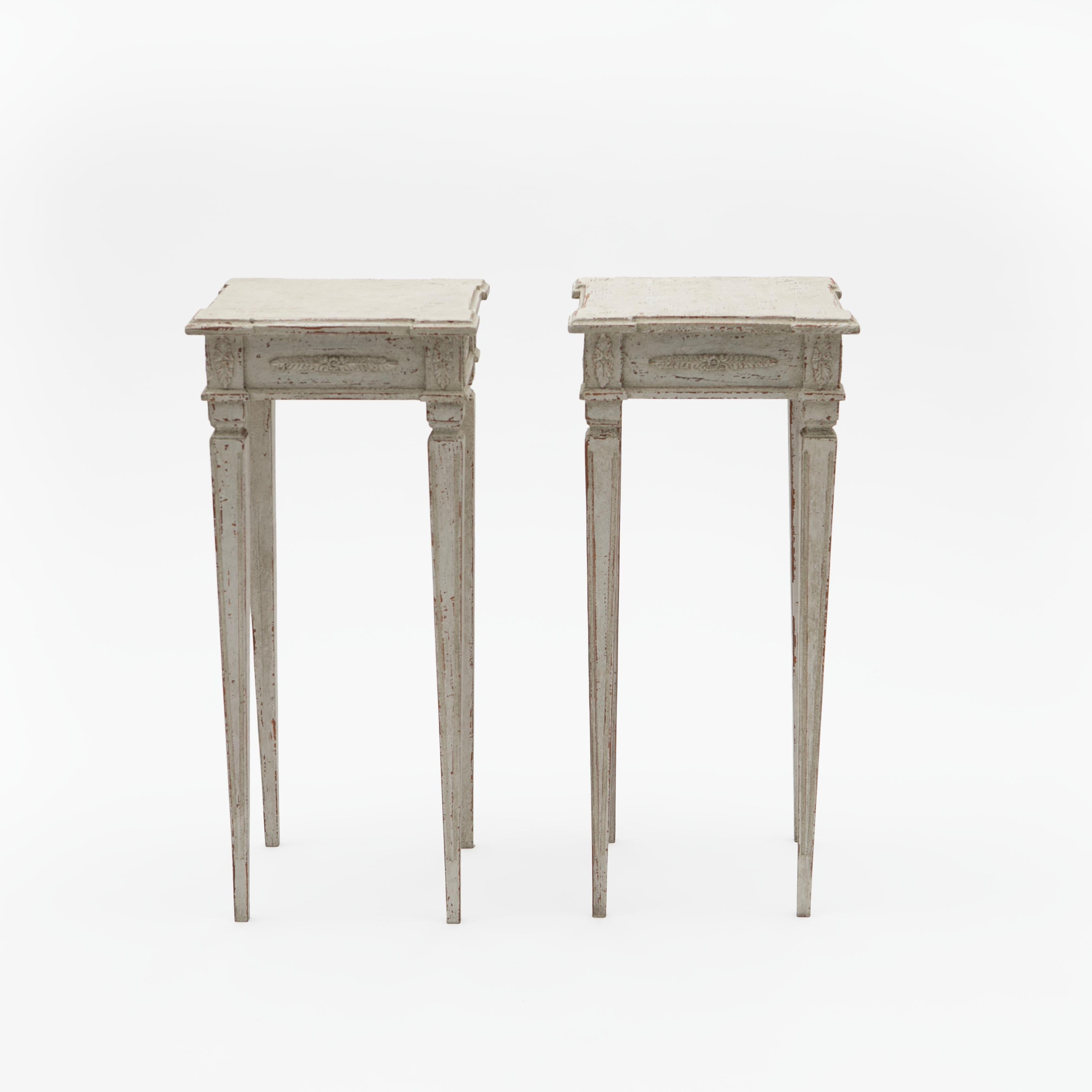 Pair of light grey painted Swedish Gustavian style side lamp tables resting on elegant narrow tapered and fluted legs.
Top with canted corners and a decorative carved skirt.

Sweden 1860-1880