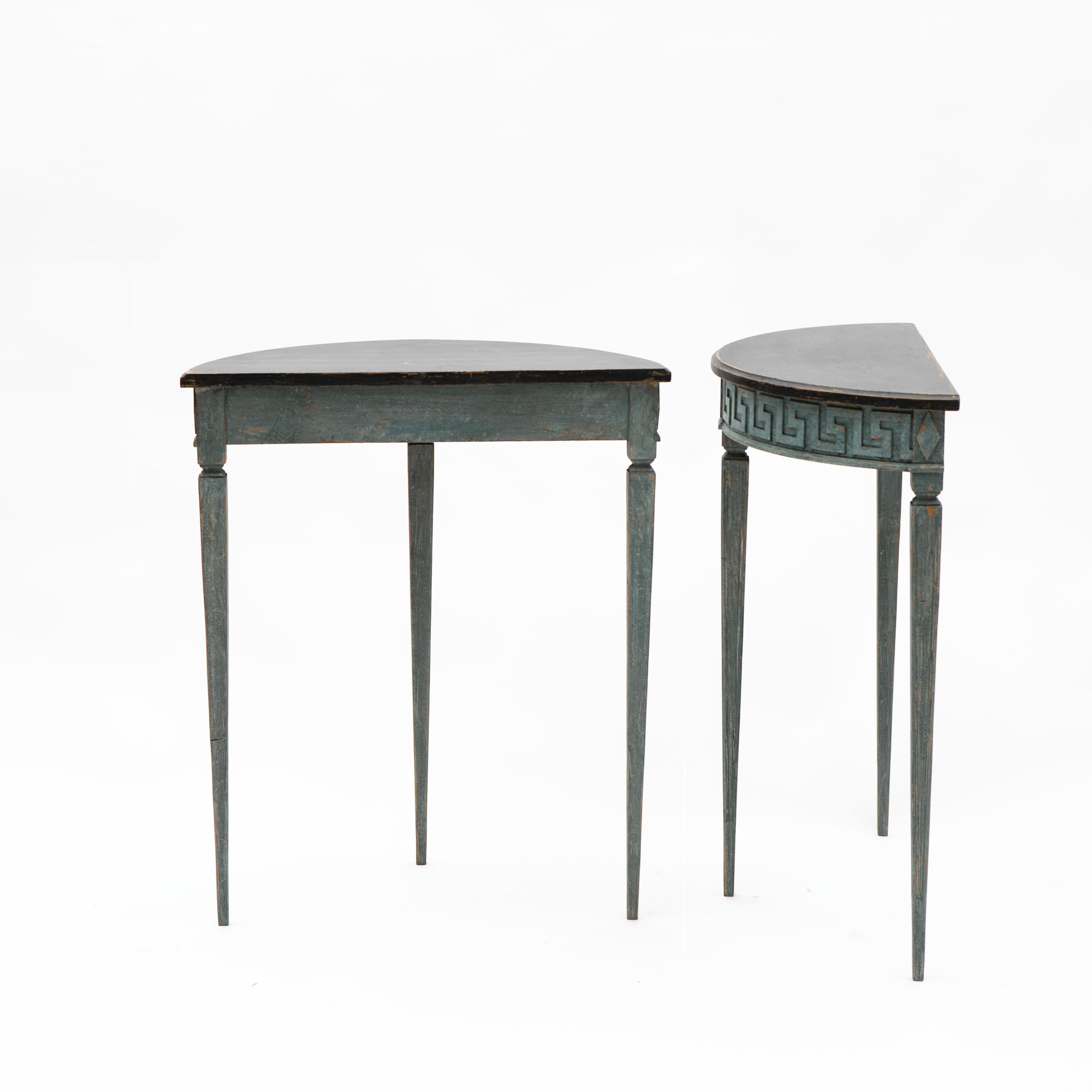 Pair of demilune console tables in Gustavian style.
Black tabletop with profiled edge. Blue-painted base with curved apron featuring carved à la grecque border and diamonds. Tapered legs with fluting.

Sweden, circa 1900.

Sold as a pair.