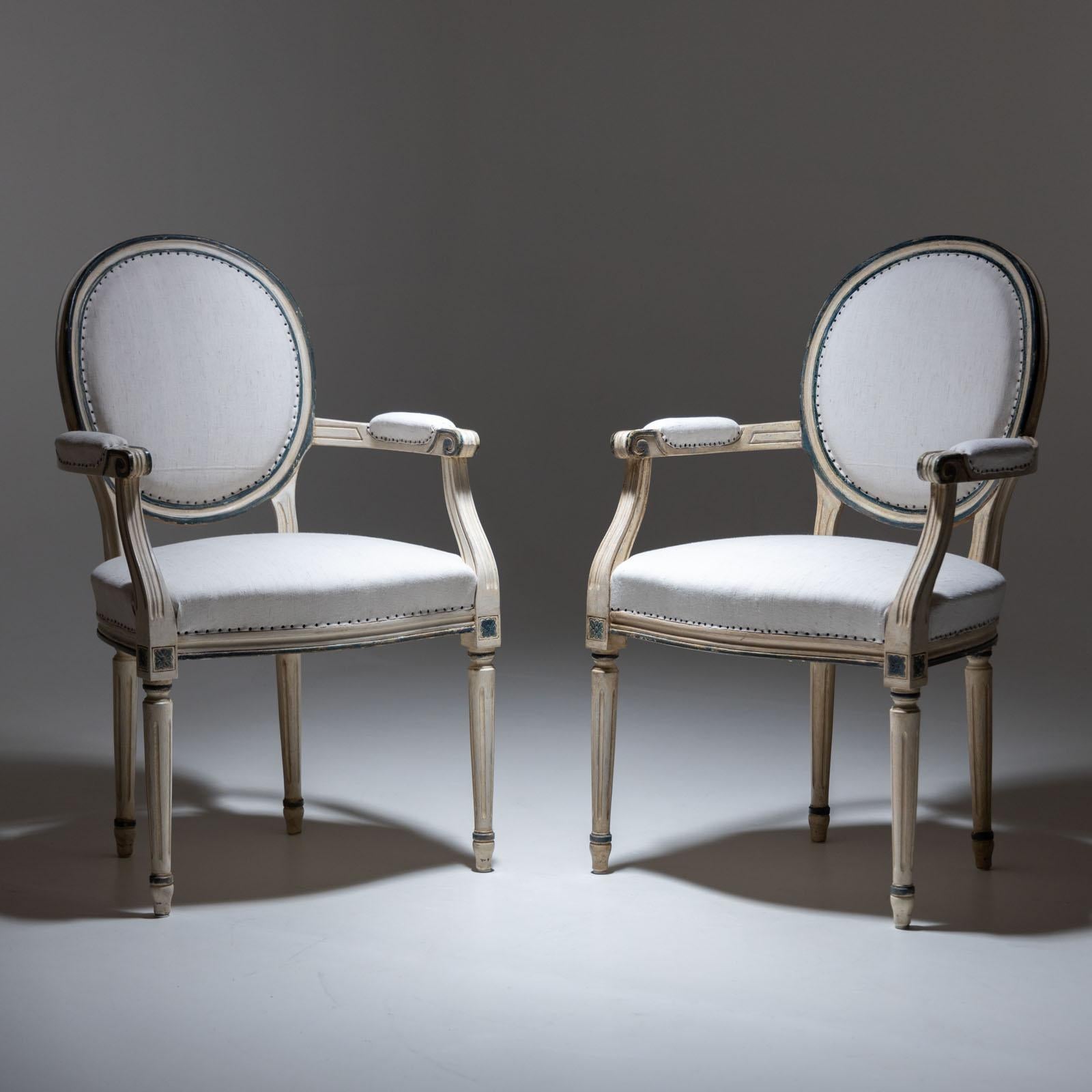 Paire de chaises avec dossiers rembourrés en forme de médaillon et accoudoirs et sièges rembourrés. La peinture beige avec des accents vert foncé est neuve et a reçu une légère patine antique. Les chaises ont été récemment recouvertes d'un tissu en