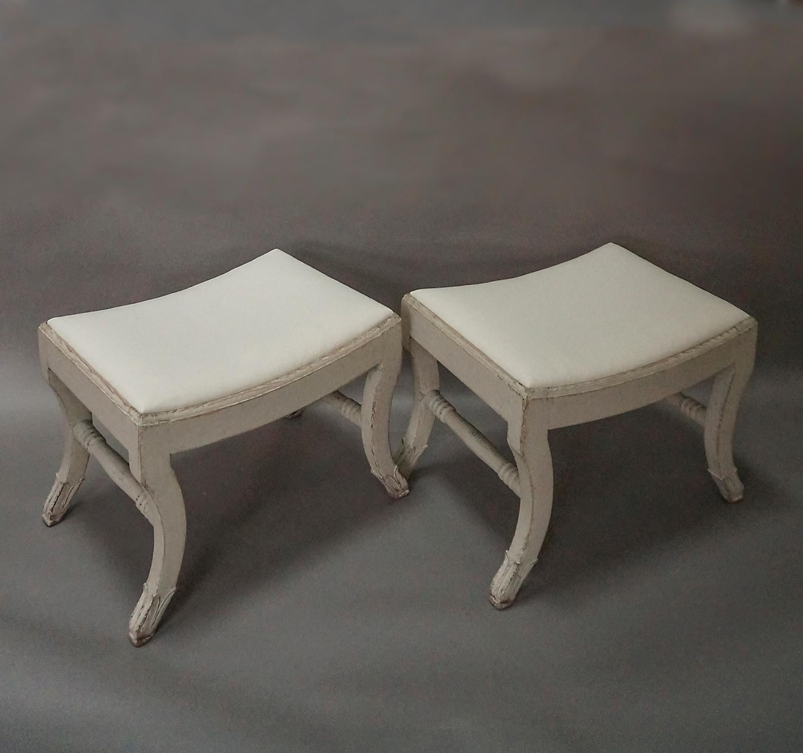 Pair of Swedish stools in the Gustavian style, circa 1910. Modified saber legs with acanthus leaf carving and turned stretchers. Slip seats and new tufted cushions.