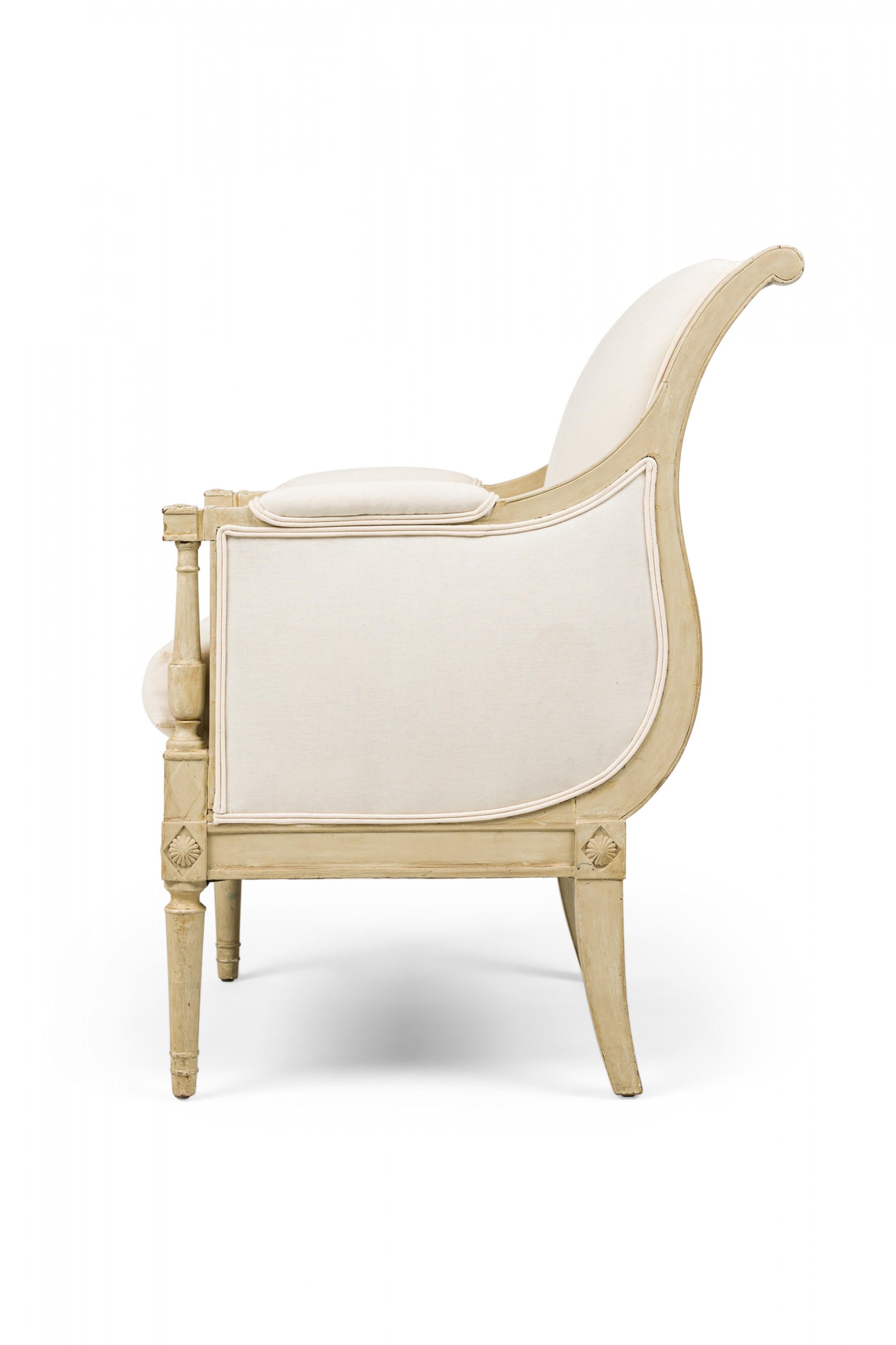 Pair of Swedish Gustavian (18/19th Century) bergere armchairs with beige painted and carved frames in Neo-classic square form upholstered in beige fabric accented by a double-piped border, resting on turned front legs and tapered squared back legs.
