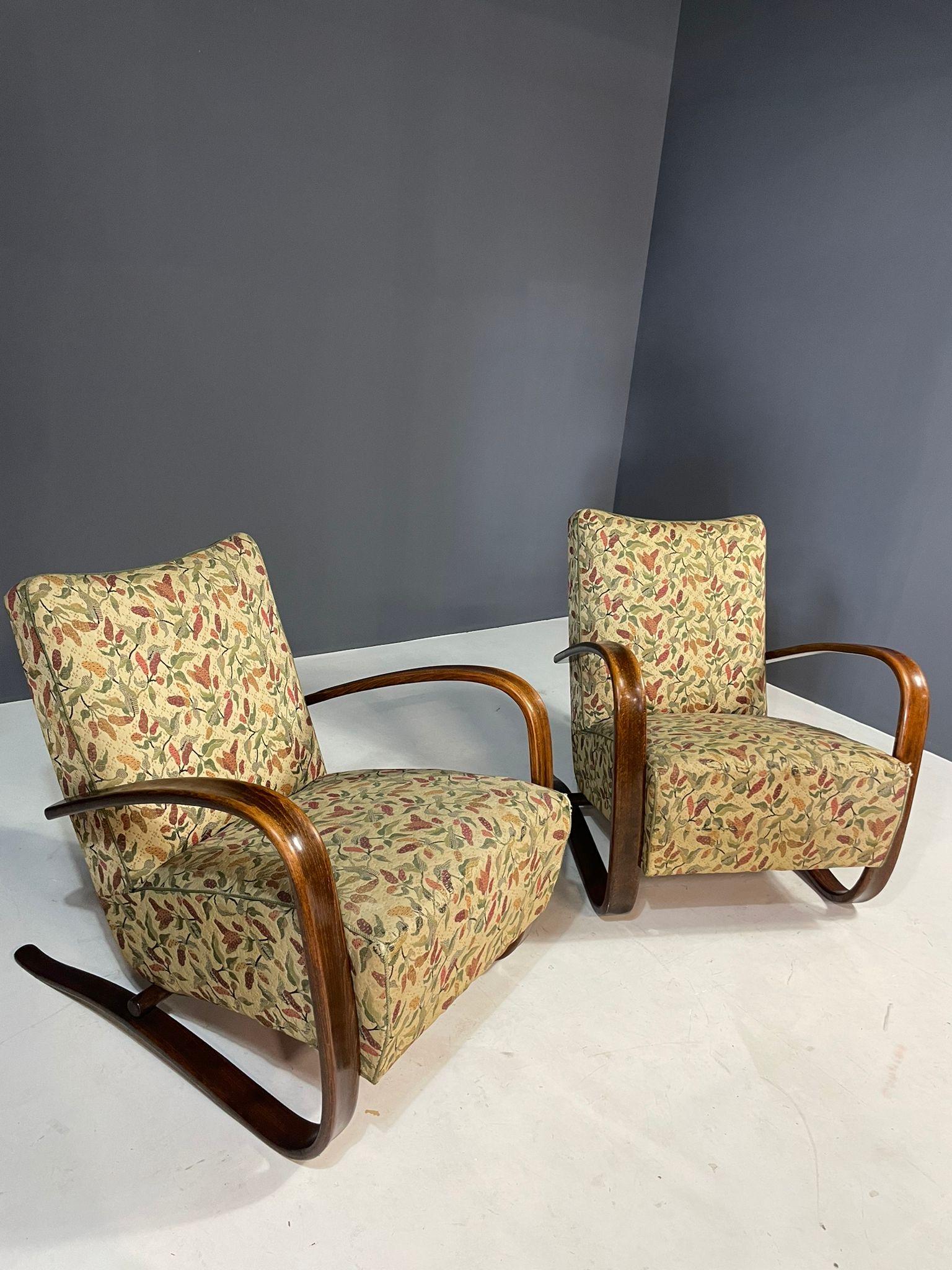 Una coppia di iconiche poltrone H269 disegnate da Jindřich Halabala negli anni Trenta. Queste sedie rappresentano l'apice del funzionalismo cecoslovacco e del design influenzato dall'Art Déco.
Presentano eleganti bracci curvi in legno di faggio