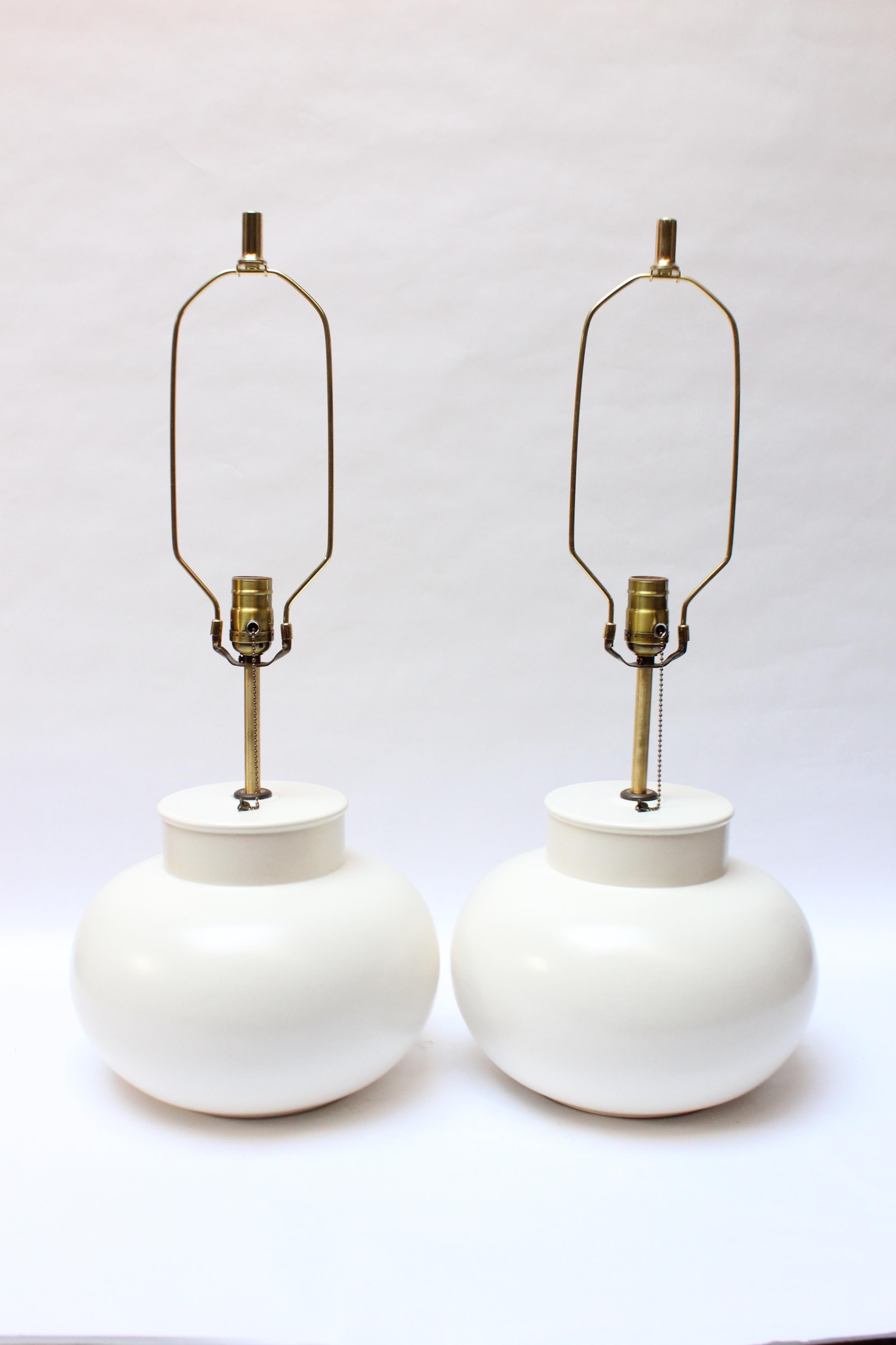 Mid-Century bulbous-form matte white ceramic table lamps by Haeger (ca. 1960s, USA). Composed of squat ceramic bases with elongated tubular brass stems. On / off switch, socket and wiring have all been replaced.
Shades are vintage and show two small