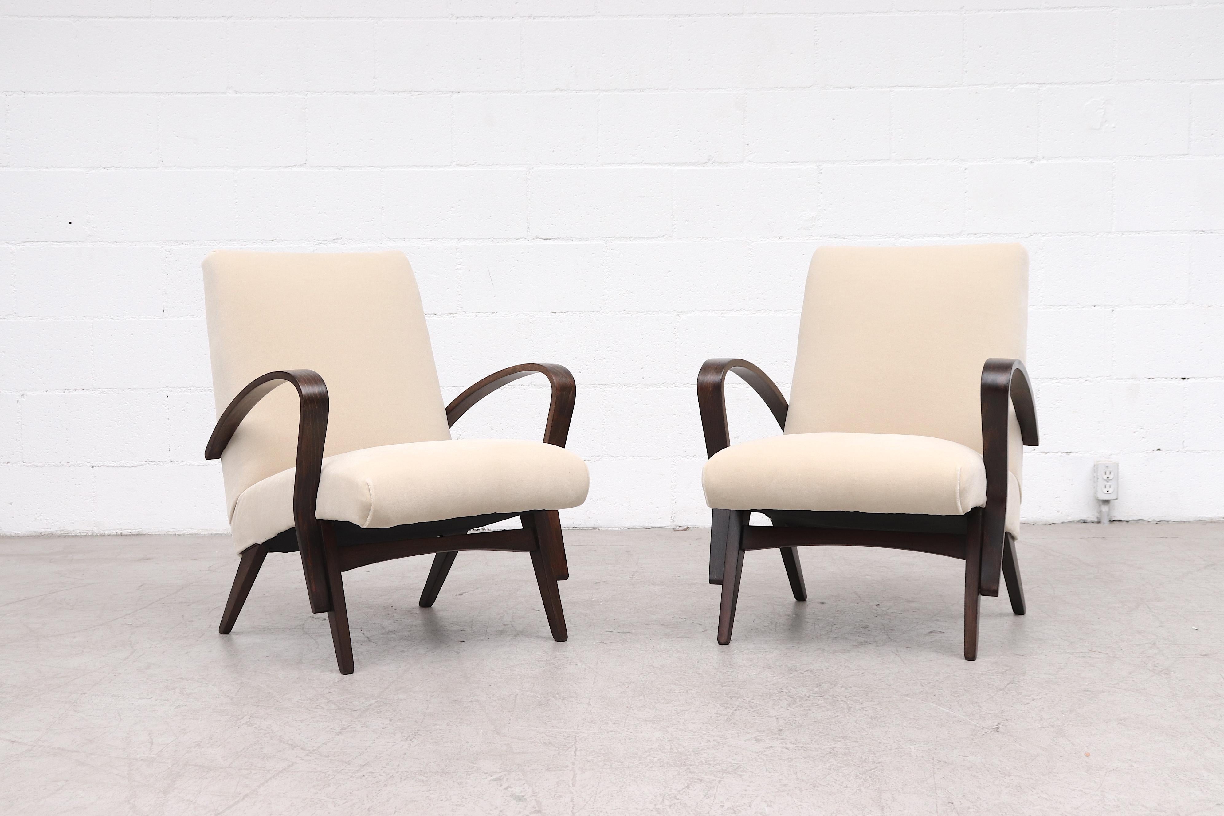 Pair of Halabala style cream upholstered lounge chairs with lightly refinished dark bent wood arms and matching tapered legs. In original condition with some visible wear consistent with age and use.
