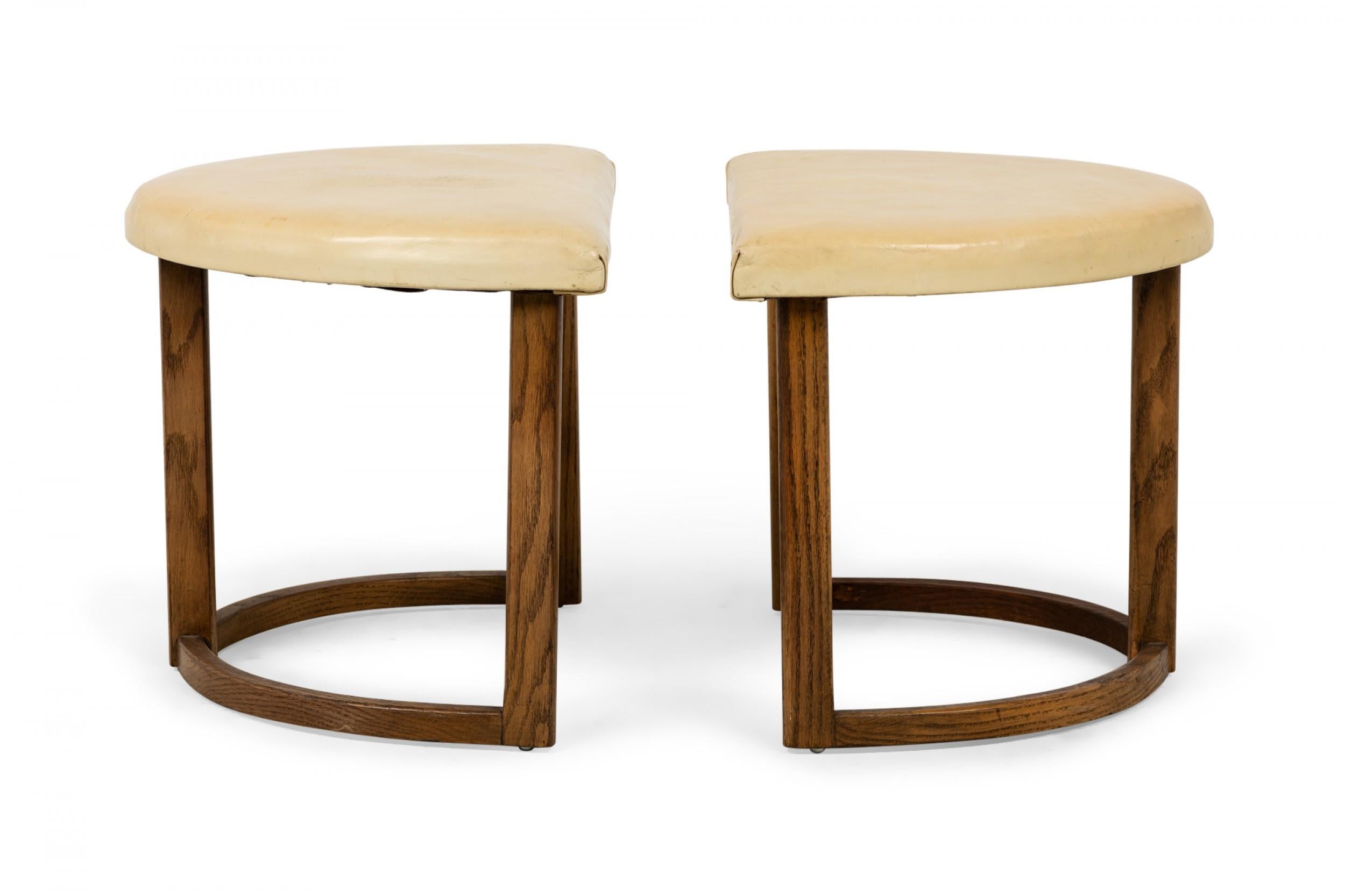 Pair of American mid-century half-moon form footstools with demilune beige leather tops resting on walnut frames with curved bases. (Priced as pair).