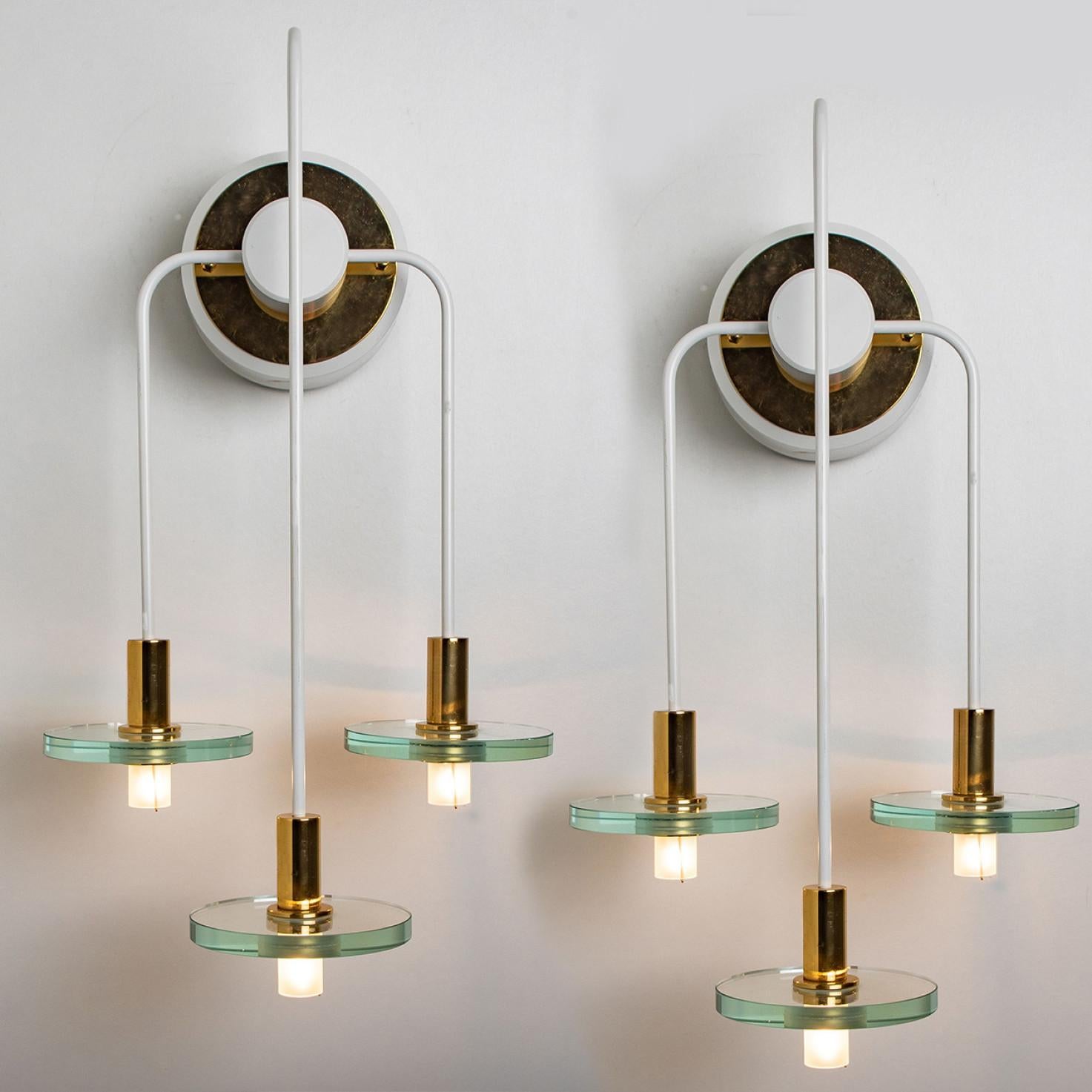 These unique wall sconces are designed and manufactured by the iconic firm of Kalmar Lighting, Germany around 1970.
They have a spacial look, because of the white metal with brass details and think glass discs.

The lights can be hung in different