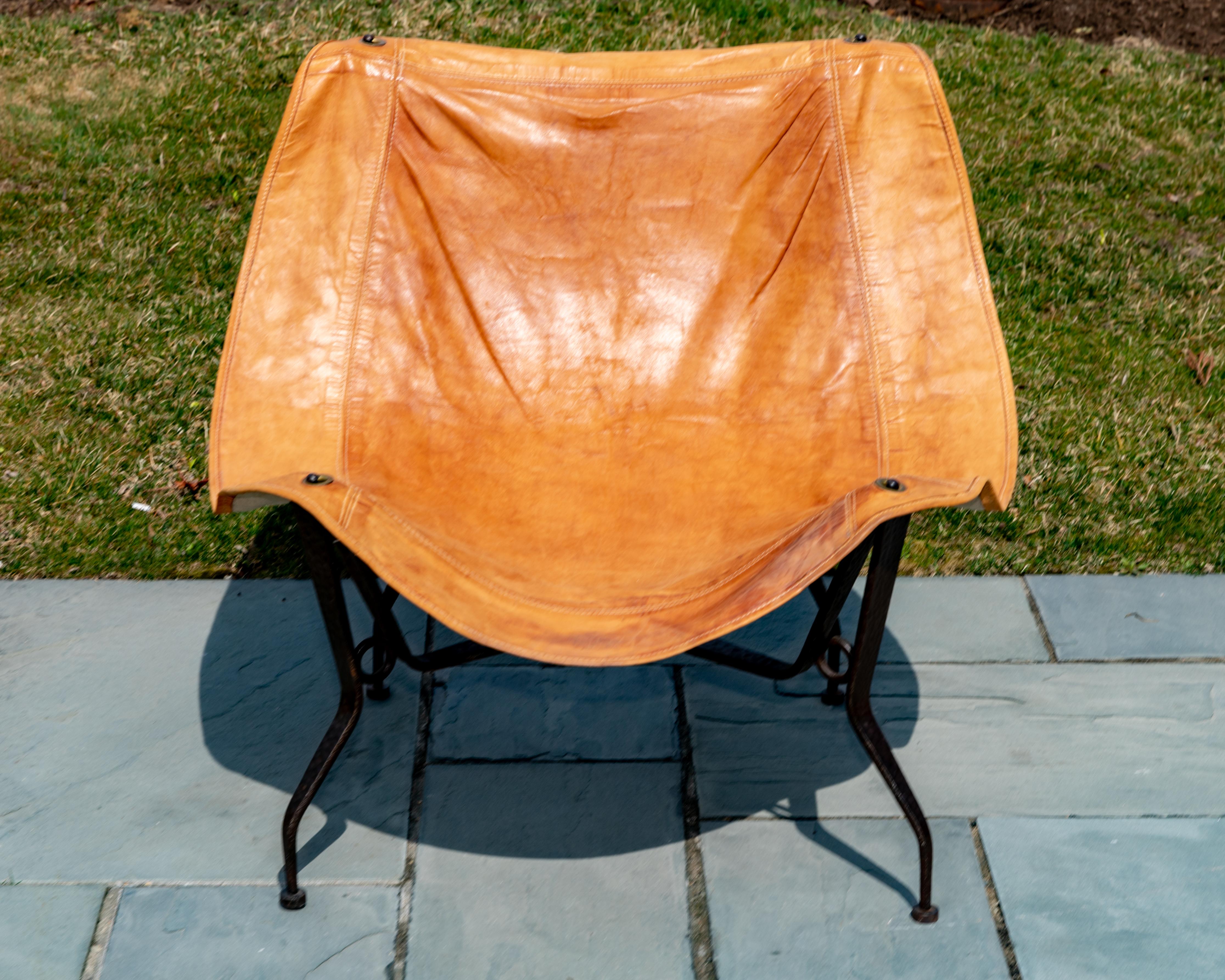 Pair of hammered frame iron chairs with suspended leather seats.