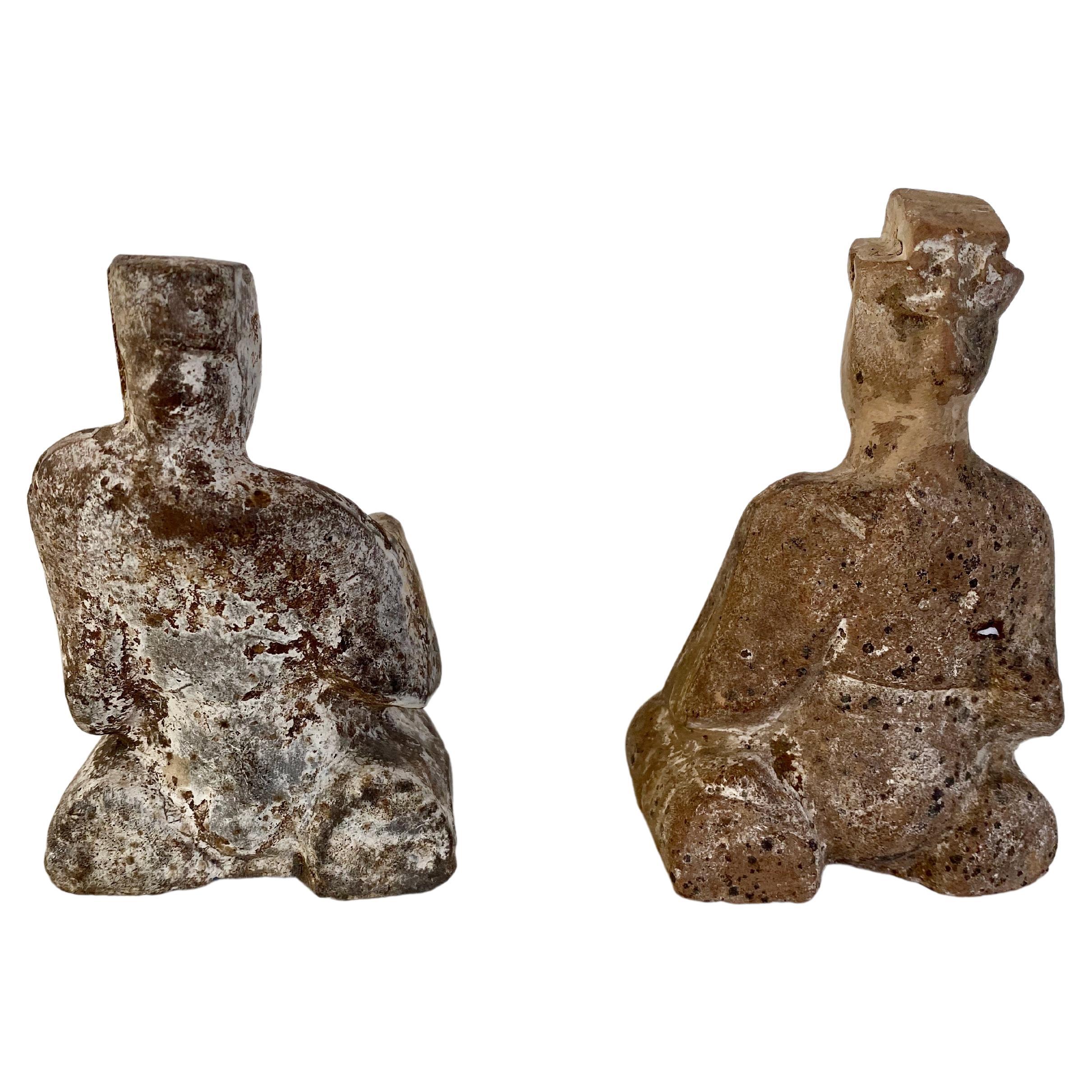 Paire de figures assises en poterie, dynastie Han (IIe siècle av. J.-C. à IIe siècle ap. J.-C.). Le plus grand des deux est assis, immobile et droit, les mains croisées dans ses manches, regardant droit devant lui. Son compagnon est affalé sur le