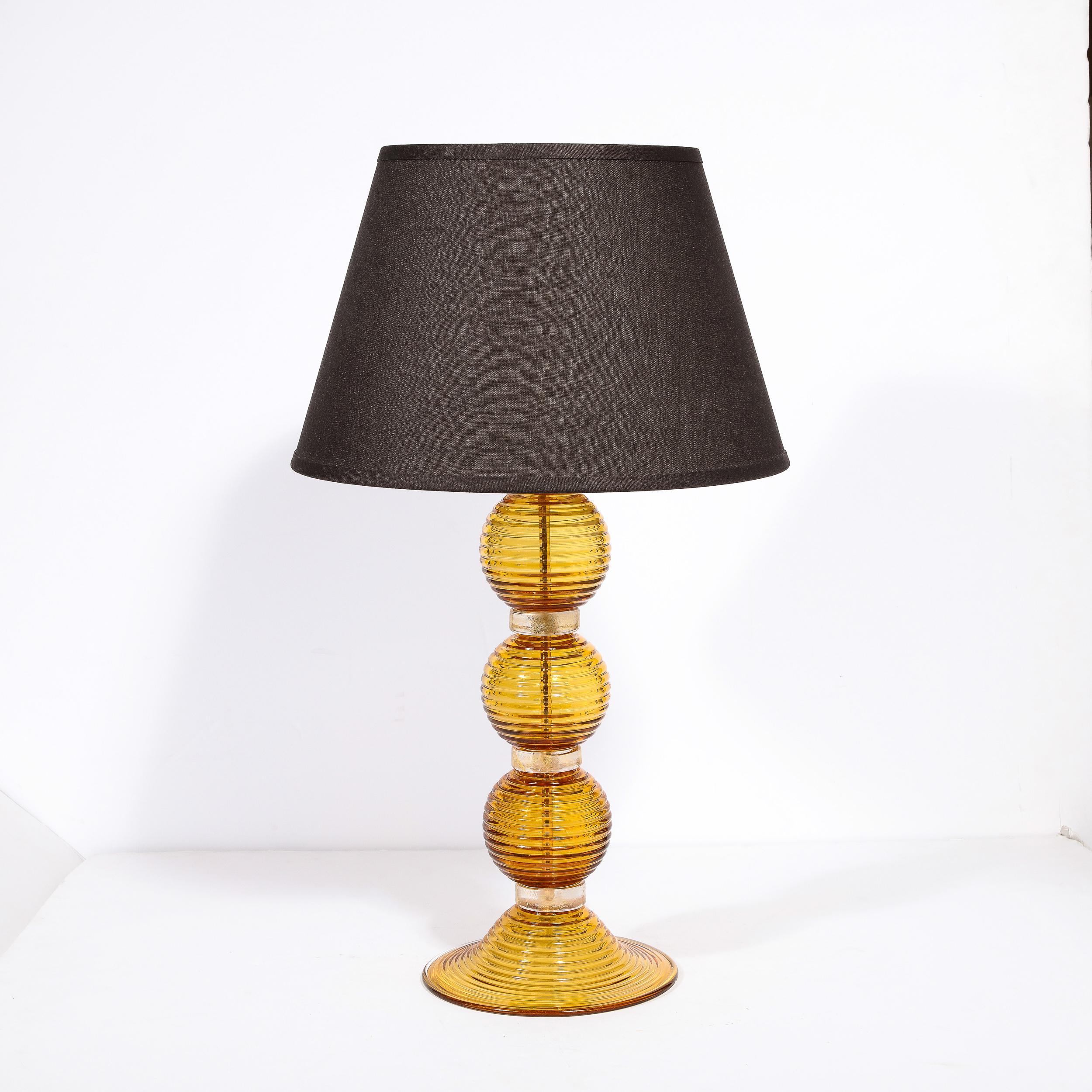 
This refined pair of table lamps were realized in Murano, Italy- the island off the coast of Venice renowned for centuries for its superlative glass production. They feature three orbital forms in a sultry semi translucent amber hued glass with