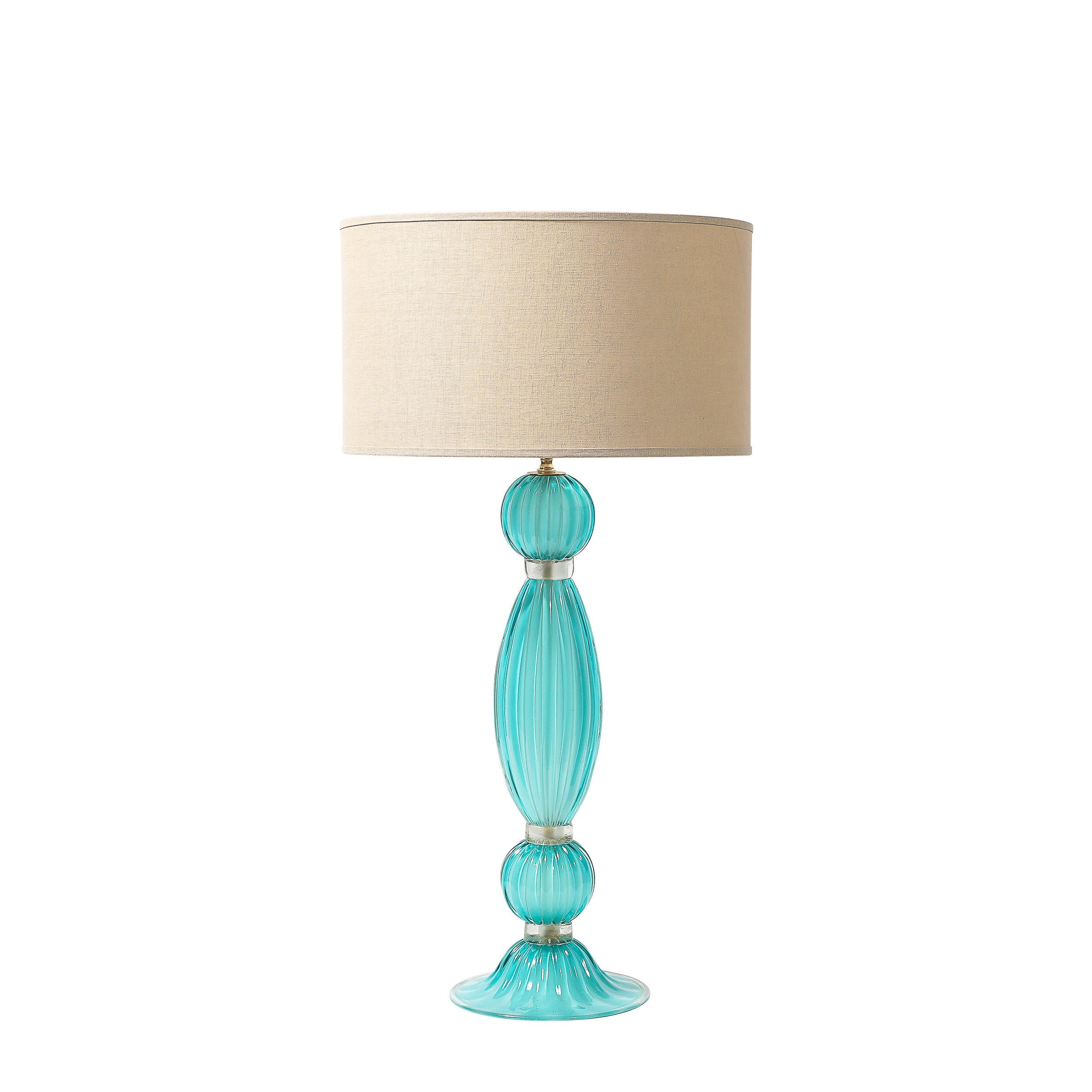 This exquisite Pair of Hand-Blown Murano Fluted Glass Table Lamps in Aquamarine Hue W/ 24 Karat Gold Fleck Banded Detailing is a perfect synthesis of Venetian craftsmanship and modern luxury. The lamps are rendered in fluted hand-blown Murano glass