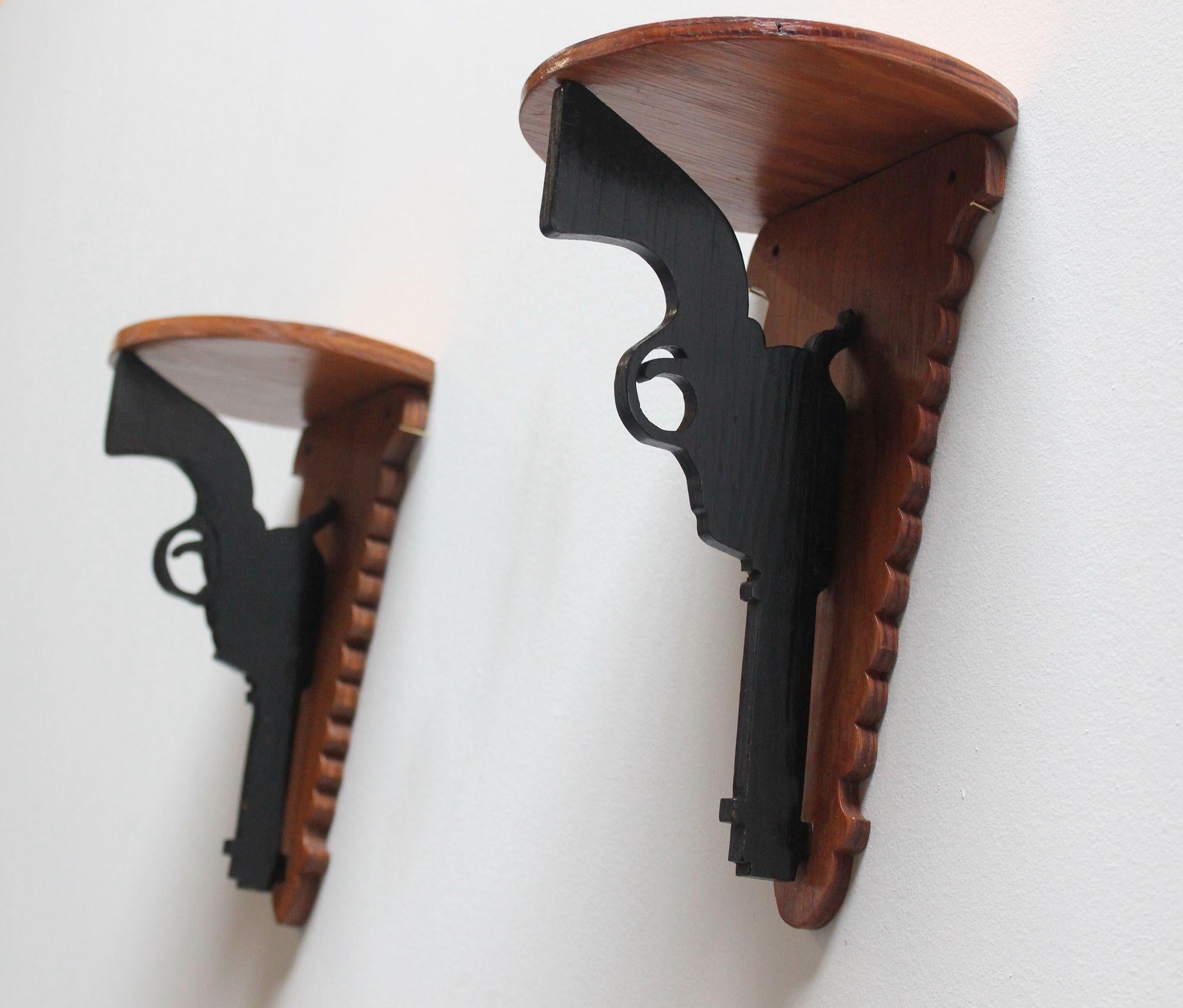 Pair of Folk Art hand-carved and painted revolver/pistol/handgun trade signs/wall brackets/corner shelves (ca. 1950s, USA).
All original black paint against stained plywood mounts supporting shallow shelf surfaces.
Very good, vintage condition with