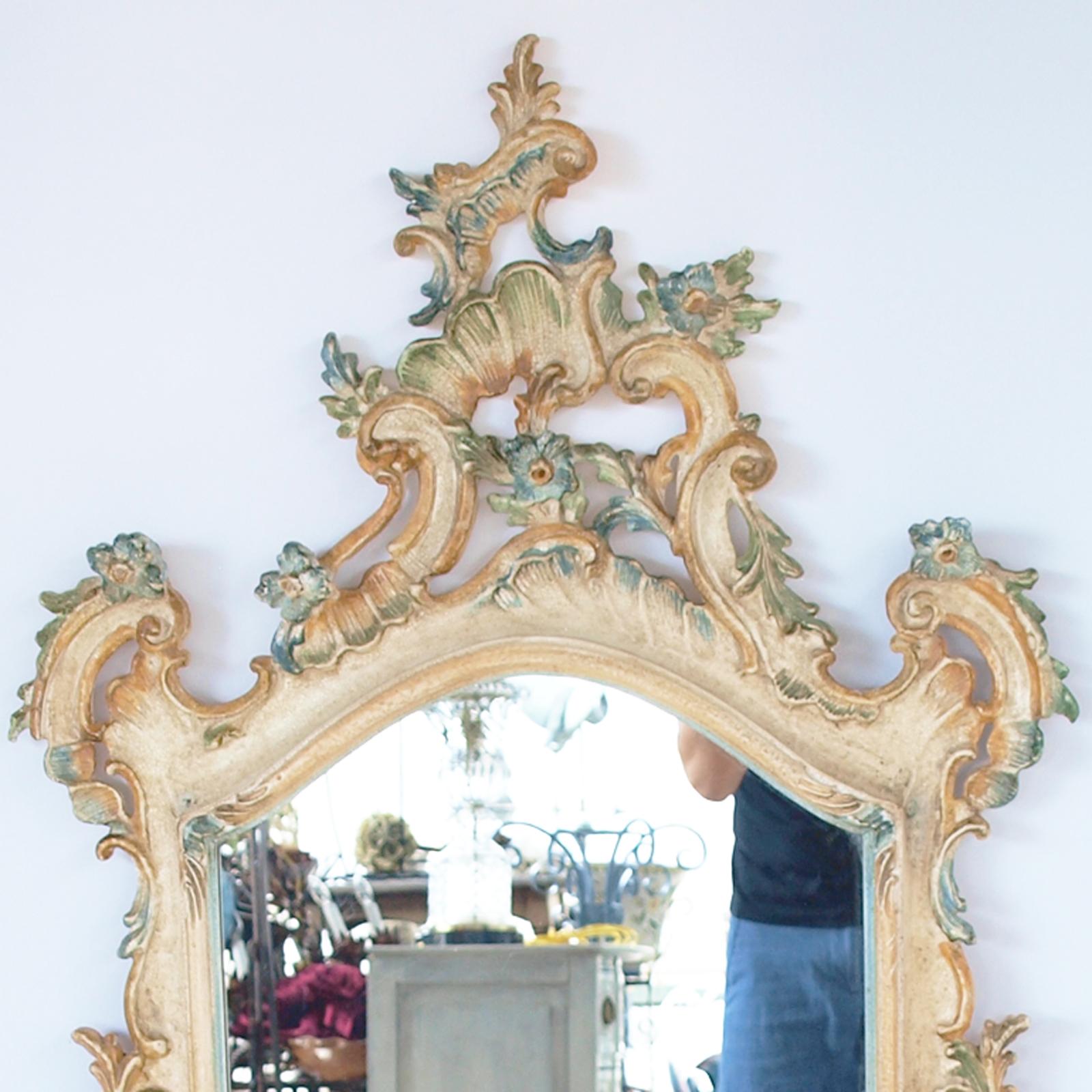 Pair of polychromed mirrors, each handpainted in pastel yellows, blues and greens, hand-carved frame in Rococo taste; each having an arched, rectangular mirrorplate behind a molded frame bordered by elaborate decoration of C-scrolls, combing,