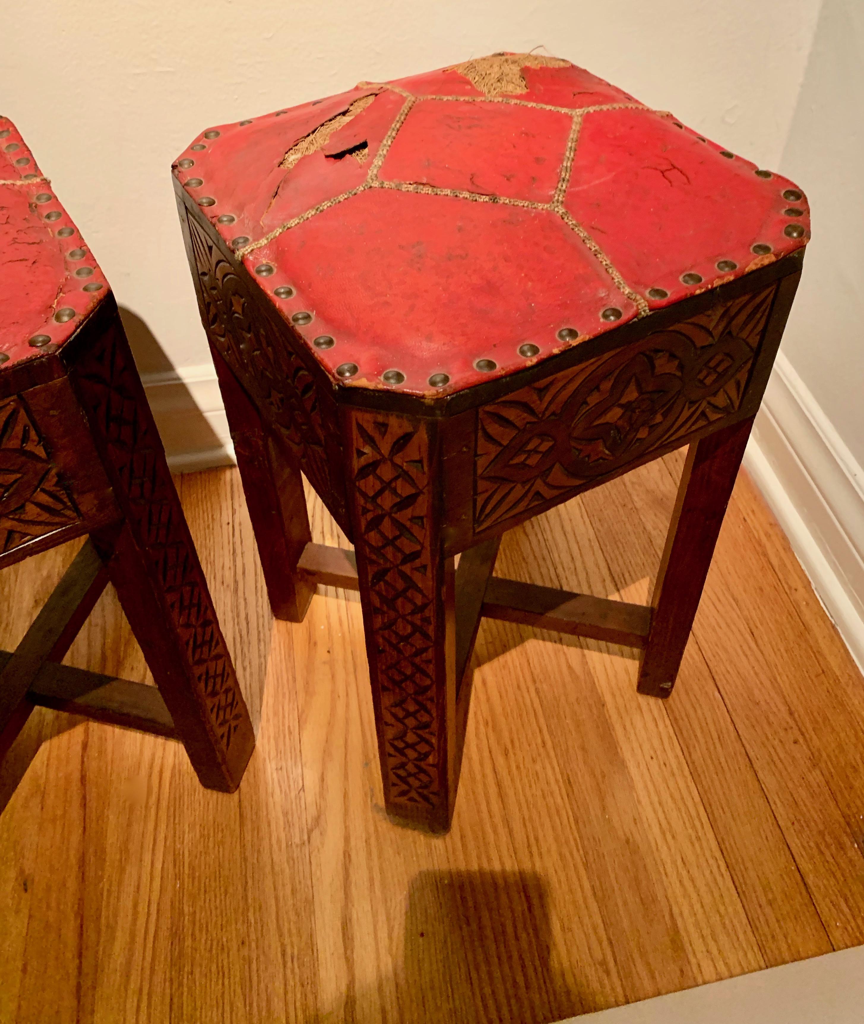 Pair of hand carved Arts & Crafts stools - the unique and rare pair have been kept in the original condition with intricate woven seams. The cracked and patinated red leather has exposed horse hair, suited for the most unique spaces. Well made and