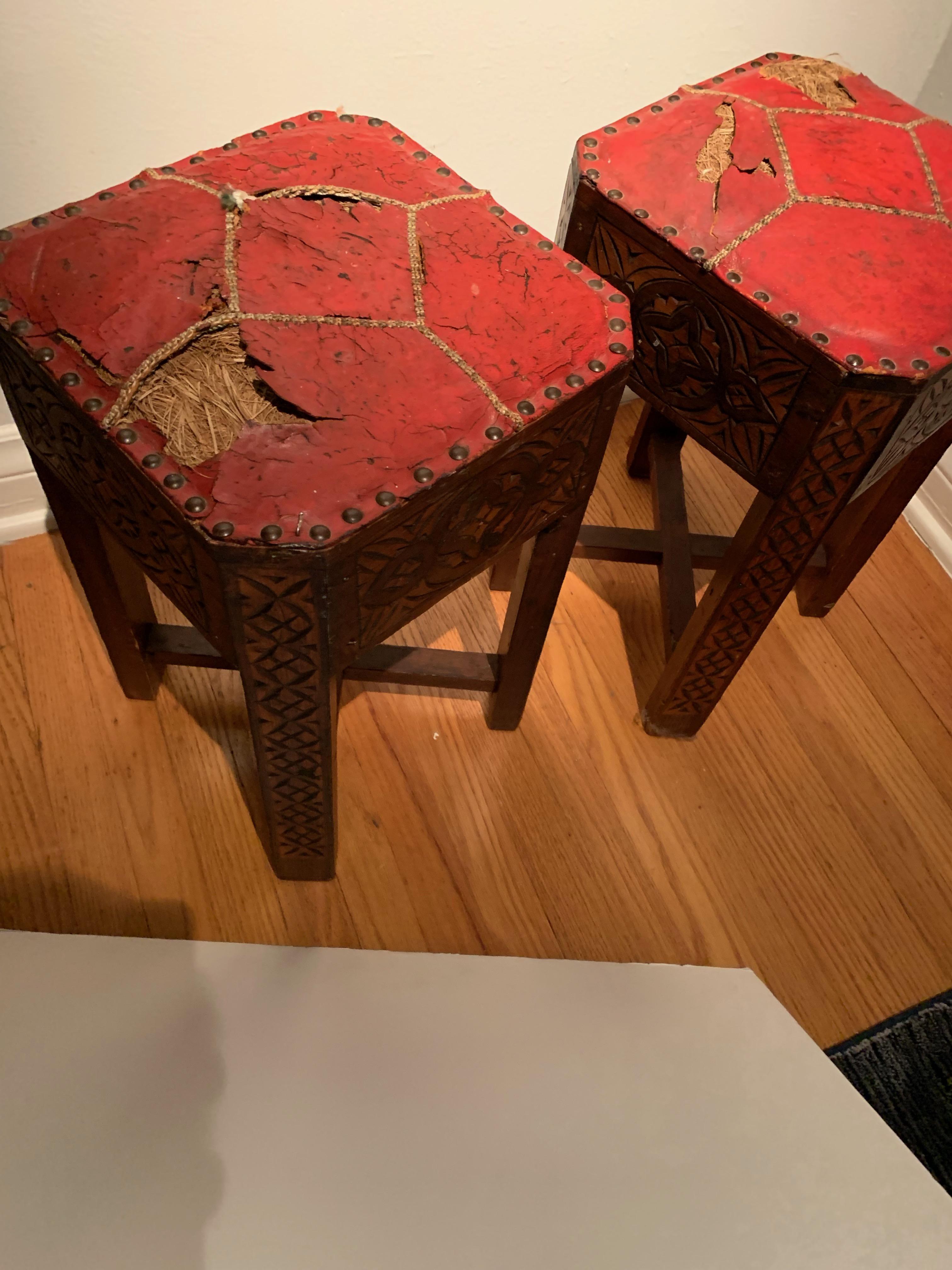 Pair of hand carved Arts & Crafts stools, the unique and rare pair have been kept in the original condition with intricate woven seams. The cracked and patinated red leather has exposed horse hair, suited for the most unique spaces. Well made and
