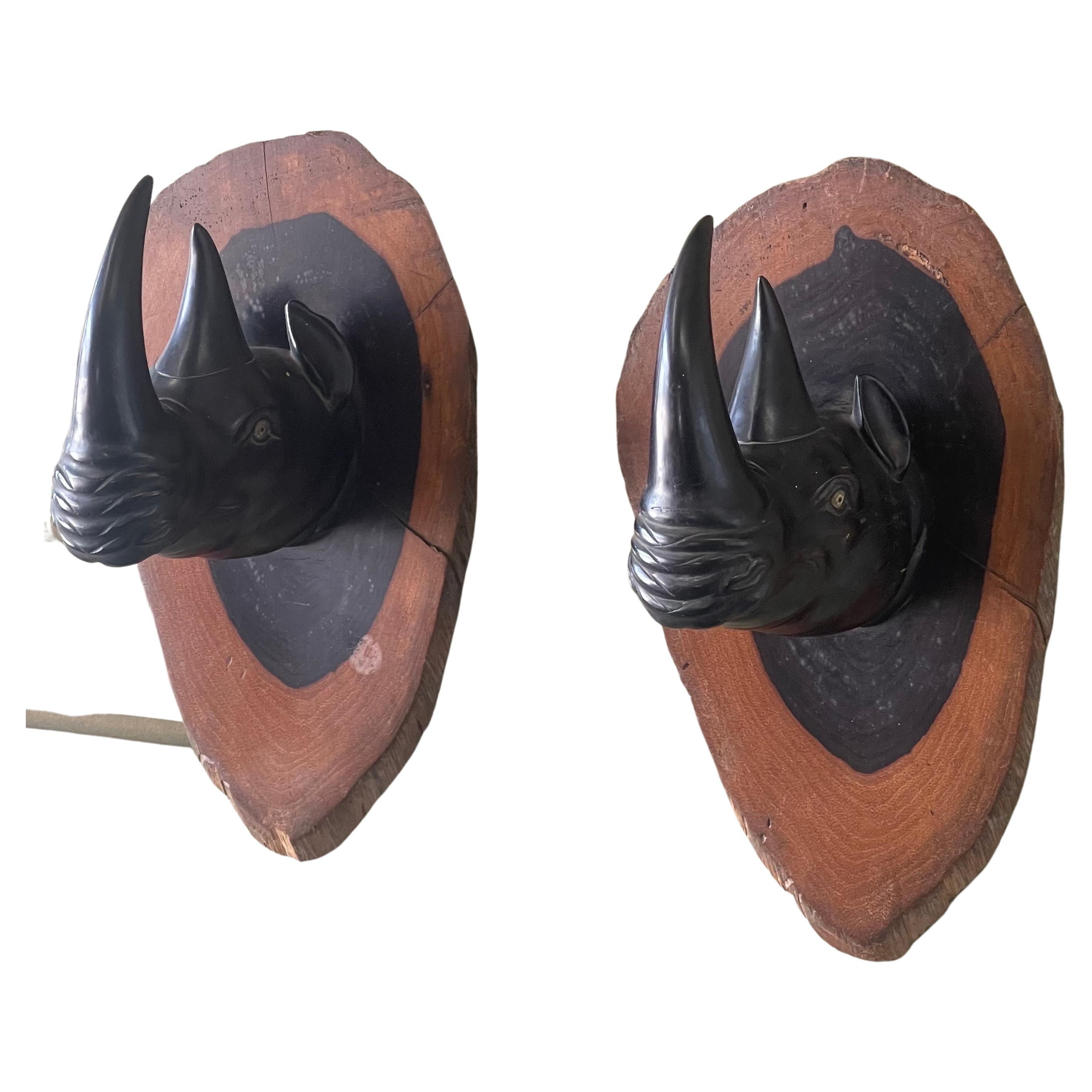 Incredibly detailed pair of hand carved ebony rhino / rhinoceros wall plaques / sculptures with glass eyes on a two tone African hardwood, circa 1970s. The plaques are extremely well made and solid; there is a metal wall hanger on the back of each