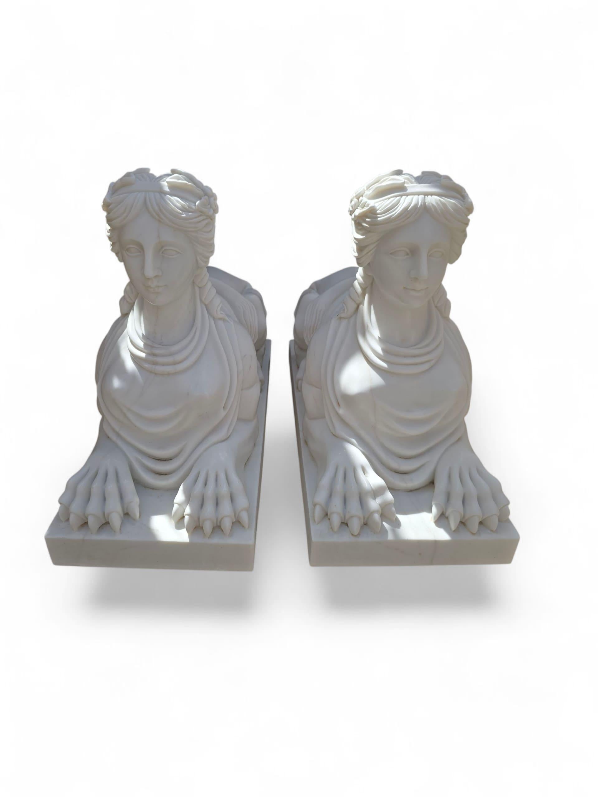 Elégante paire de sculptures de sphinx de style égyptien, taillées à la main dans du marbre blanc italien au cours du XXe siècle. Chaque figure présente le corps traditionnel du lion avec un visage humain serein, évoquant l'iconographie égyptienne
