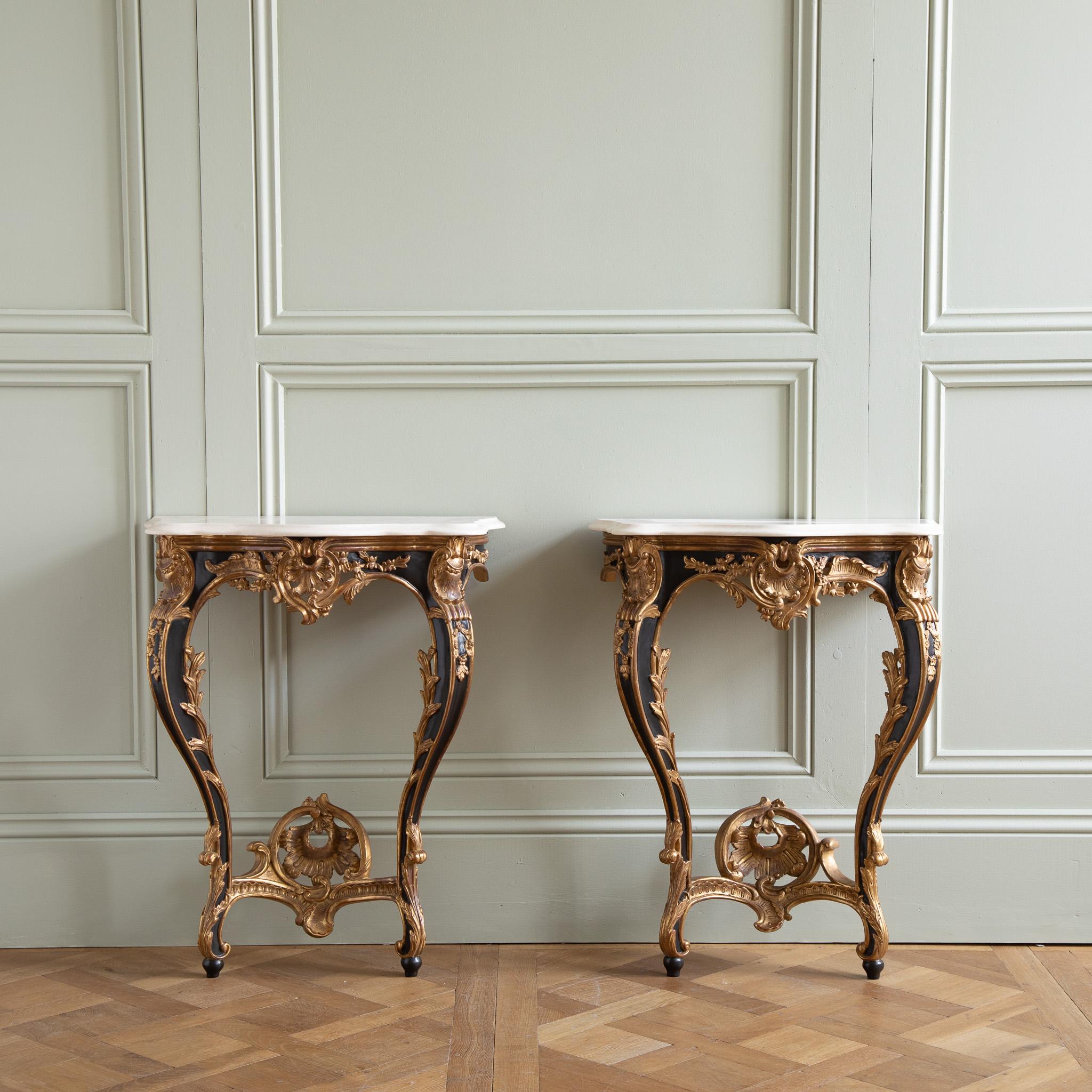 A pair of Louis XV style consoles, hand-carved by master craftsmen and finished in a hand lacquered with gold highlights, slightly aged and distressed patina. Includes a bevel-cut Crema Marfil marble which has been honed and lightly polished.