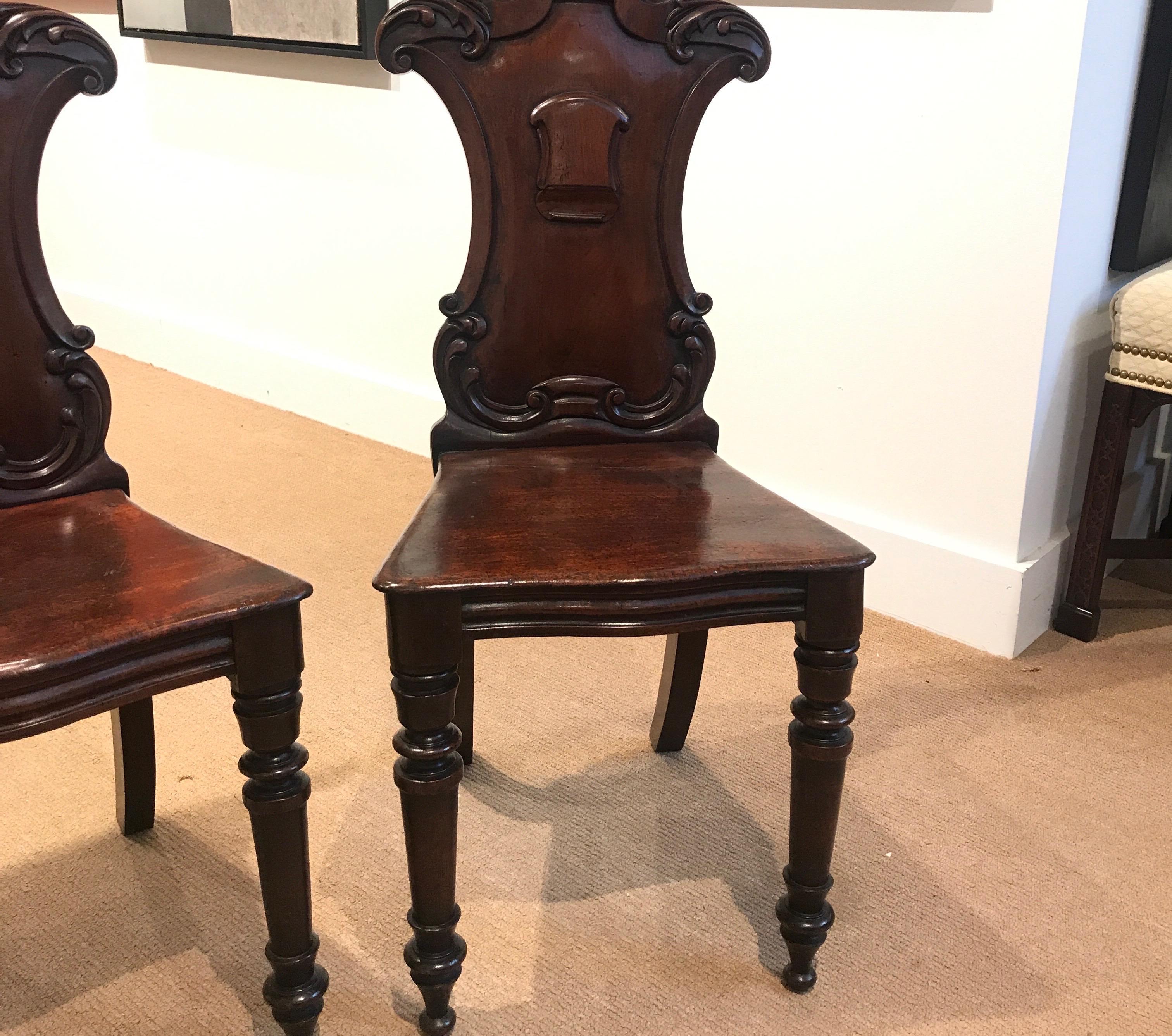 Beautifully carved mahogany hall chairs with armorial backs, hand-turned legs and solid mahogany seats. The chairs with original finish which have been French polished to show a warm, well cared for age appropriate finish, England, circa 1870-1880.