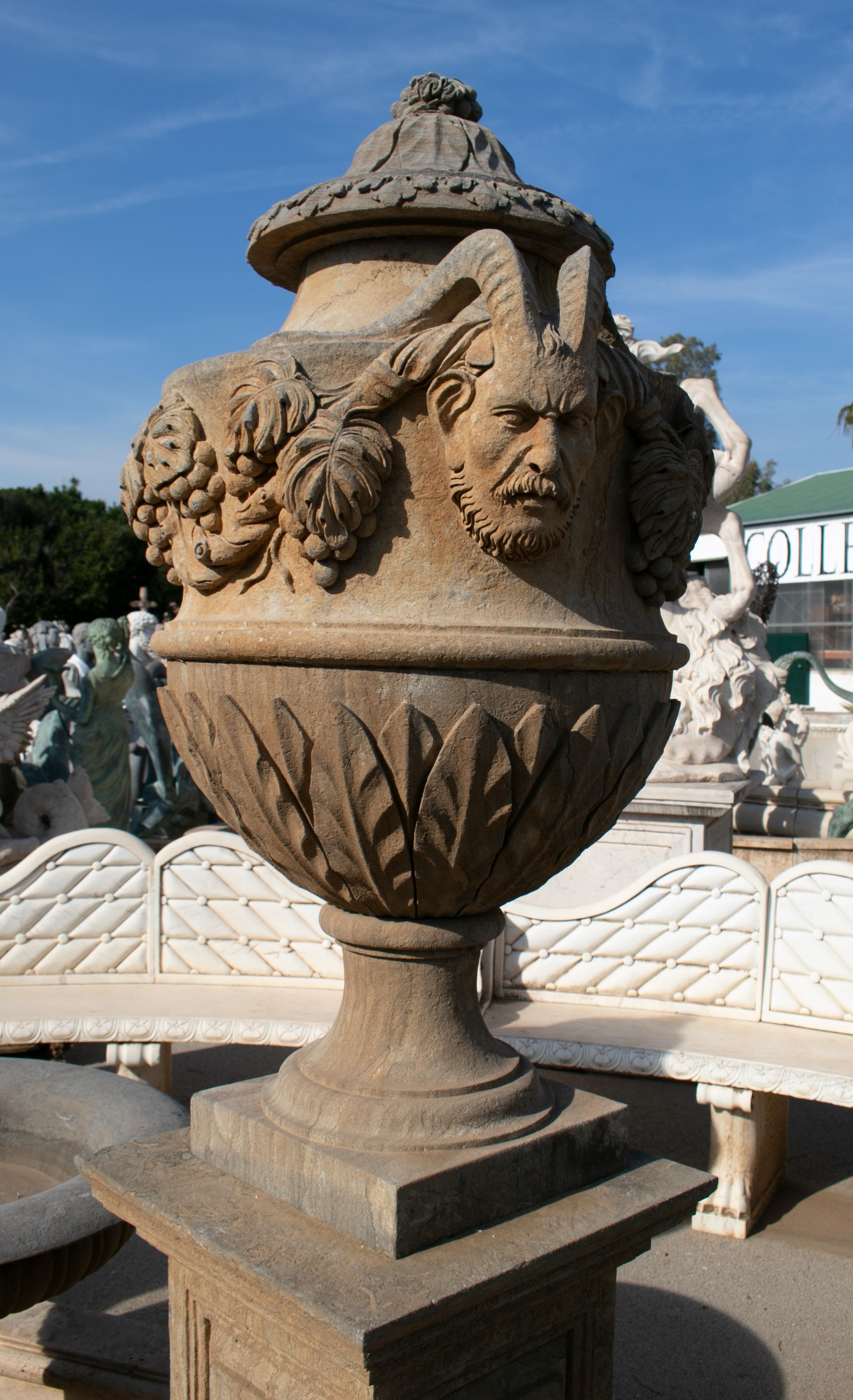 Pair of hand carved marble urns on pedestals with antique patina finish. The urns are decorated with vegetable relief and fawn head handles.