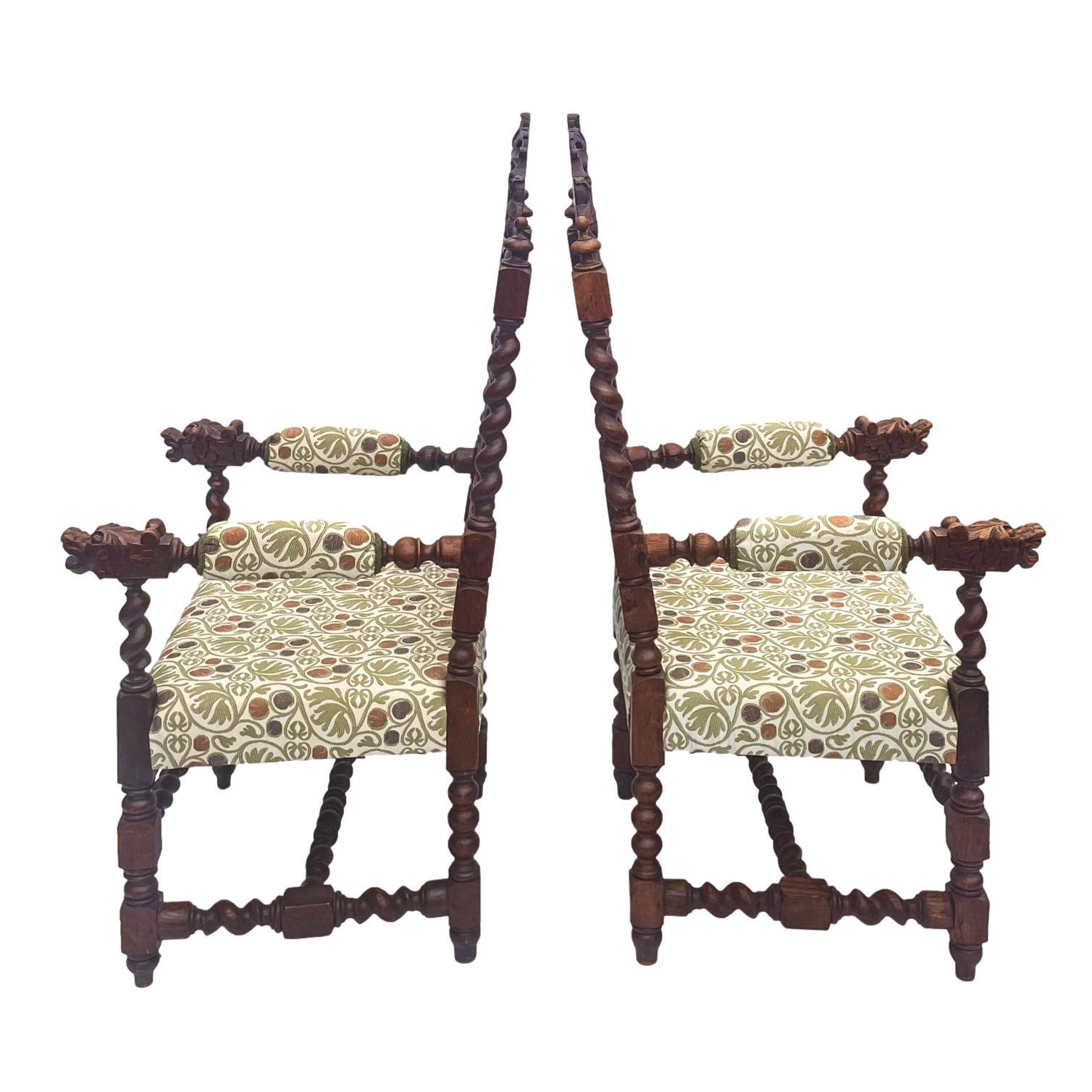 A pair of oak armchairs carved with grotesque carved heads, barley twist turned posts, and stretcher base, the caned backs framed by foliate carving and further barley twist turnings terminating with finials, English, circa 1880.