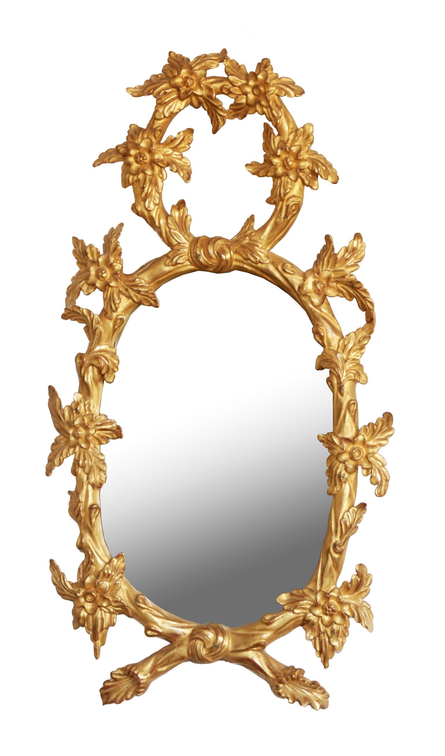 A pair of oval hand carved mirrors made in the English period style of George III featuring a naturalistic theme of curved branches embellished with leaves and open blossoms. The pieces have been hand gilded in 23.75-karat gold leaf and burnished to