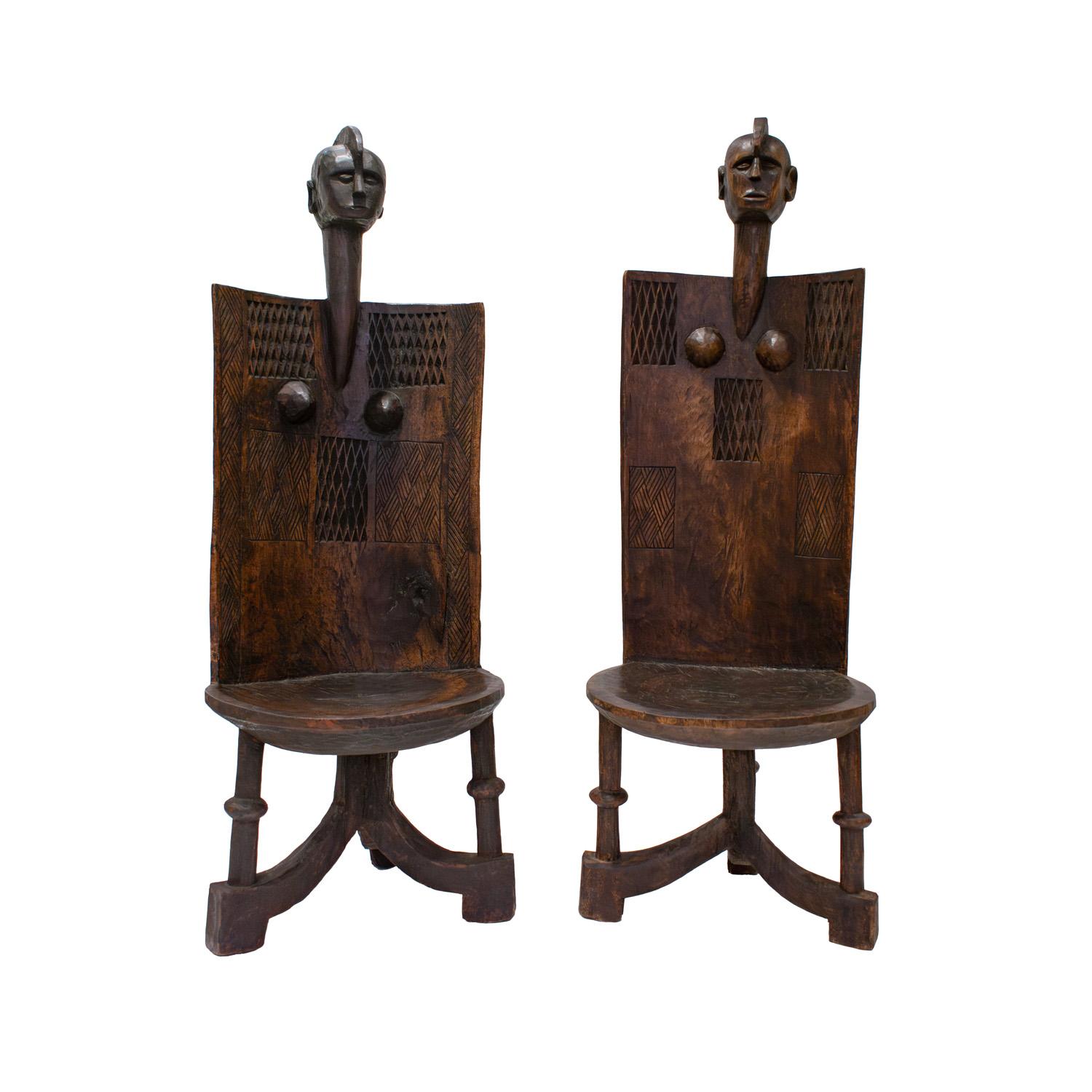 Large tribal carved wood chairs with figural mask crests, curved back with breasts and geometric carved elements on front and back and solid seat rising on hewn legs, likely from Tanzania, East Africa 1960s. These chairs are beautifully made and