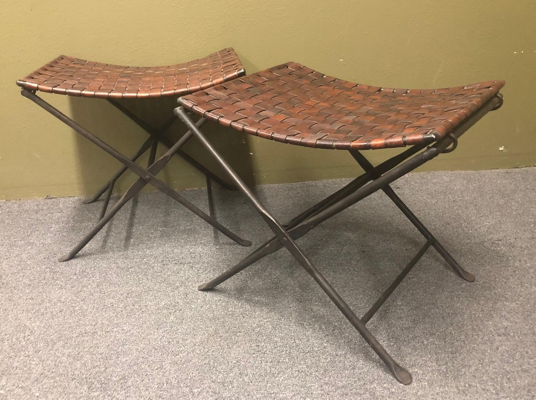 A striking pair of hand forged wrought iron and woven brown saddle leather folding stools / benches, circa 1970s. Solid, heavy and functional; great addition to any room!