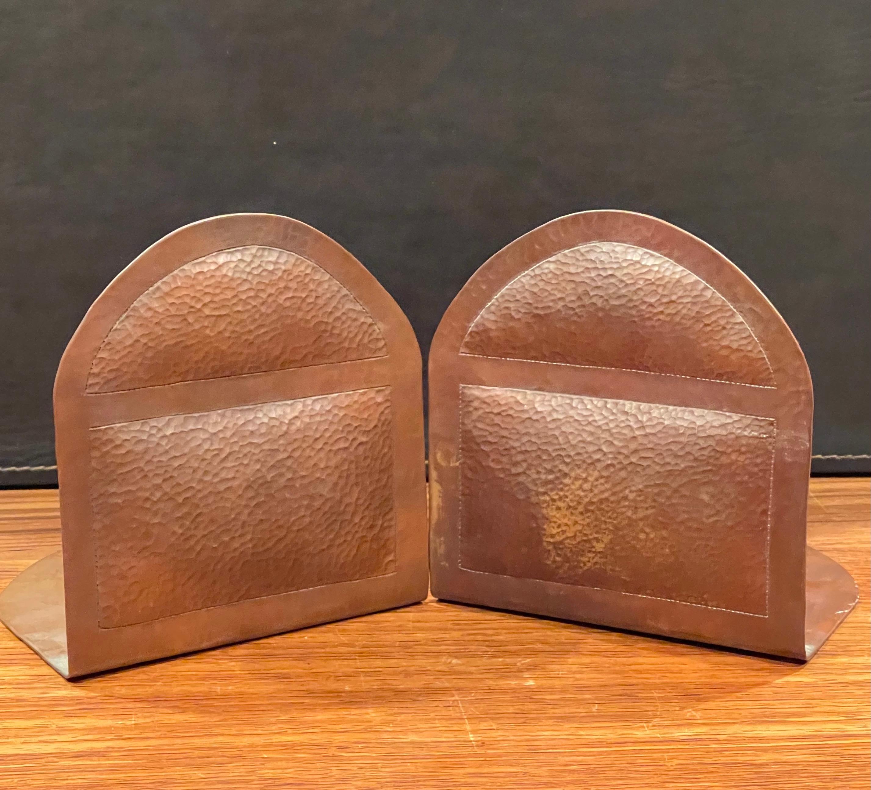 Pair of hand hammered copper Arts & Crafts style bookends by Ramiro M., circa 1980s. The pair are in very good vintage condition and have a simple arch design and a wonderful patina. Each bookend measures 5.75