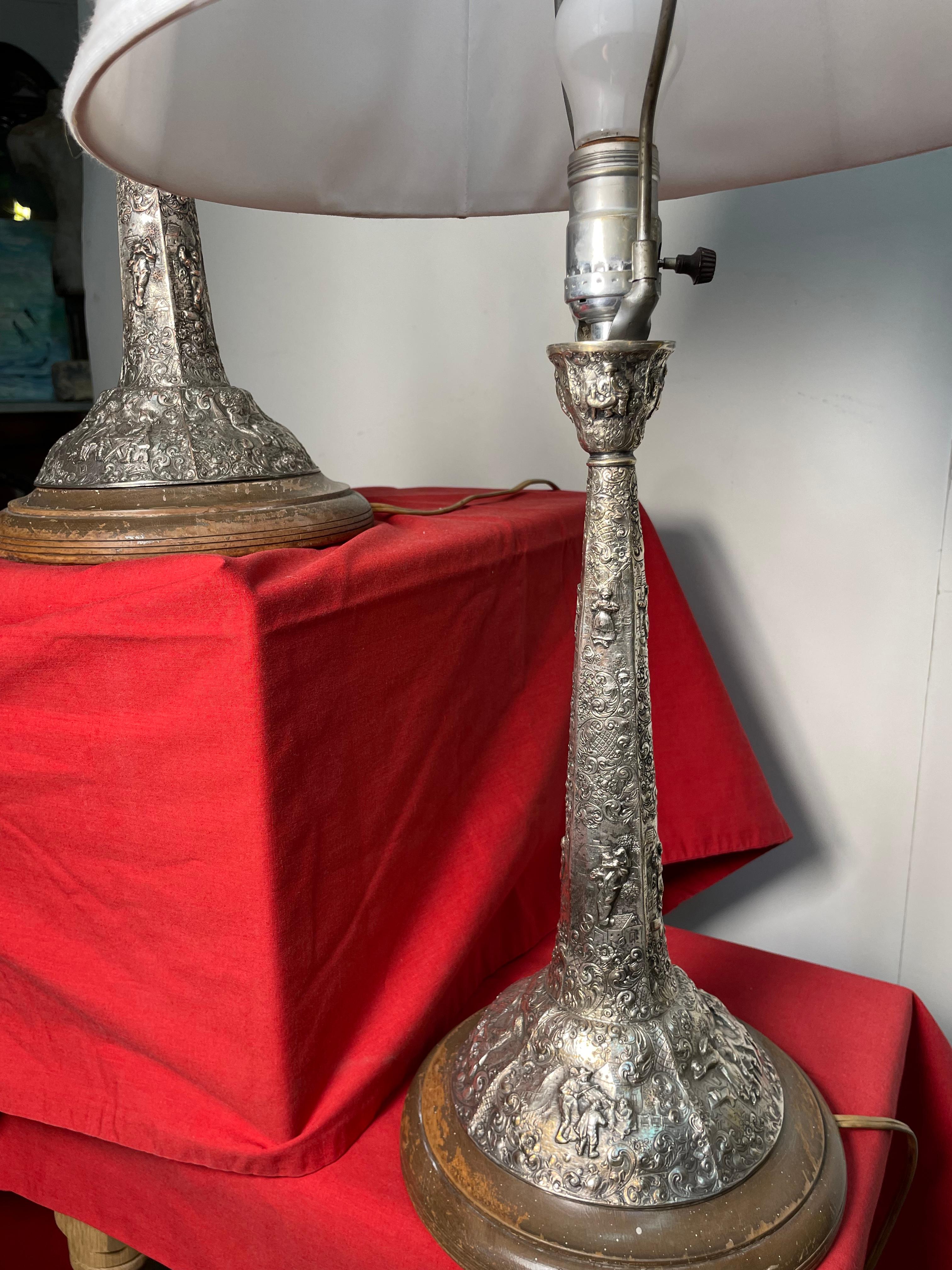 These solid silver lamps were hand hammered/carved creating an extremely detailed stand. Within the carvings you can see a depiction where there is a village and its people. The scene is set to be joyful, with the people playing music and dancing.