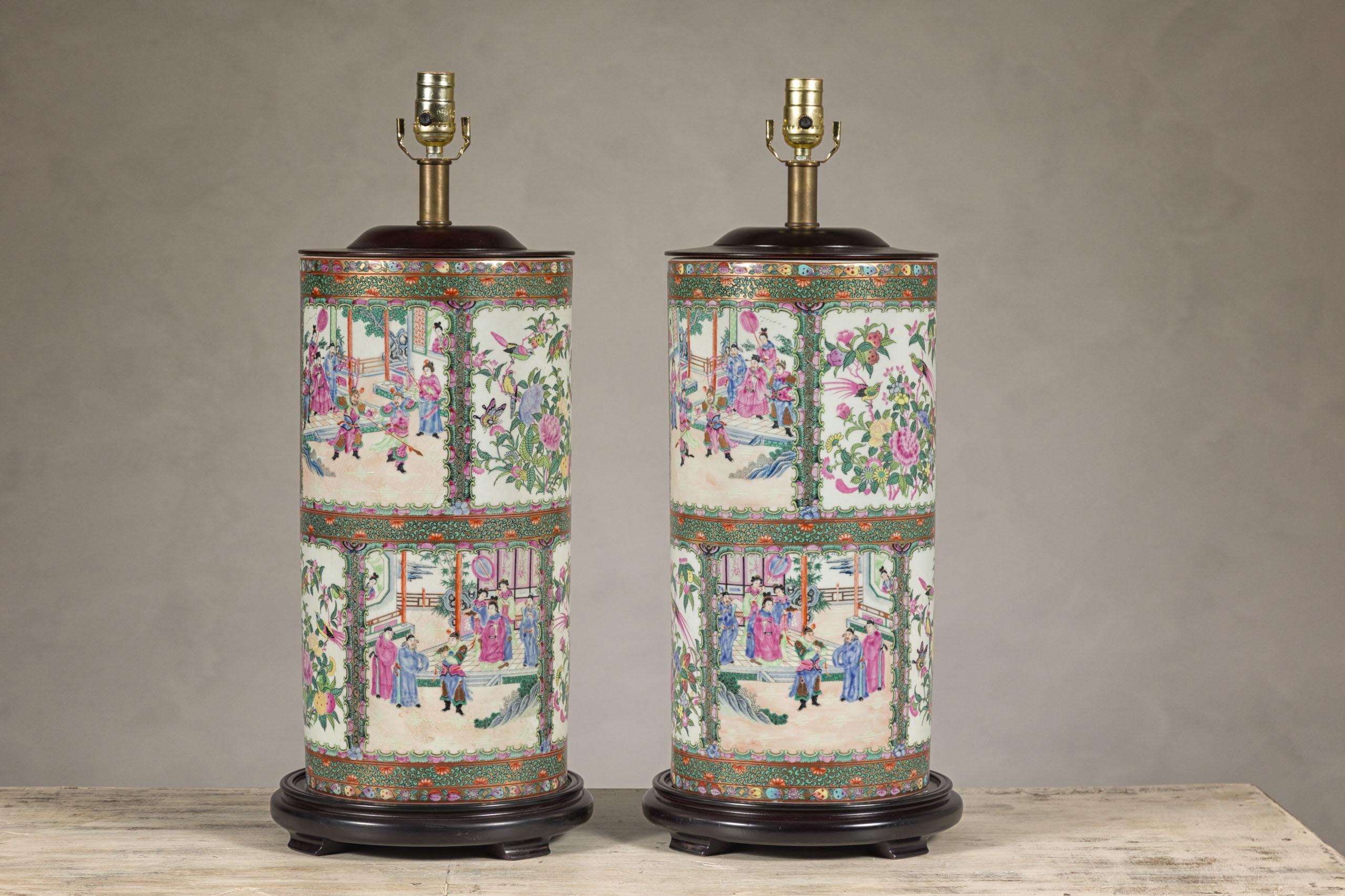 A pair of vintage hand-painted rose medallion Chinese table lamps depicting court scenes, birds and flowers in green, pink and white inset panels. Immerse yourself in history with this pair of hand-painted rose medallion table lamps, a testament to