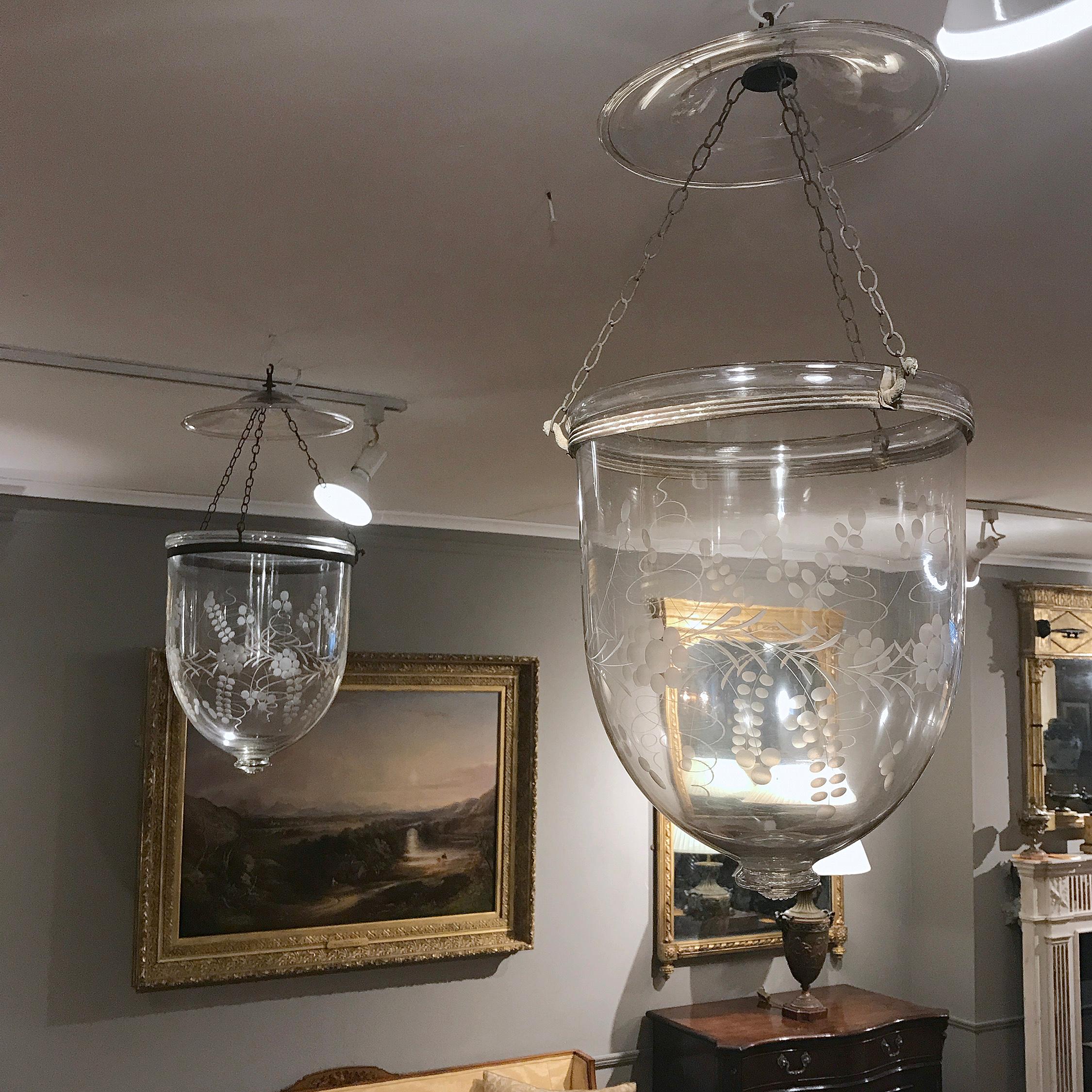 Each of these beautiful 19th century handblown glass bell jar lanterns is ornamented with an etched grape-and-vine motif. Three chains from the glass smoke bell and brass canopy attach to peacock-shaped hooks on the original rolled brass band,
