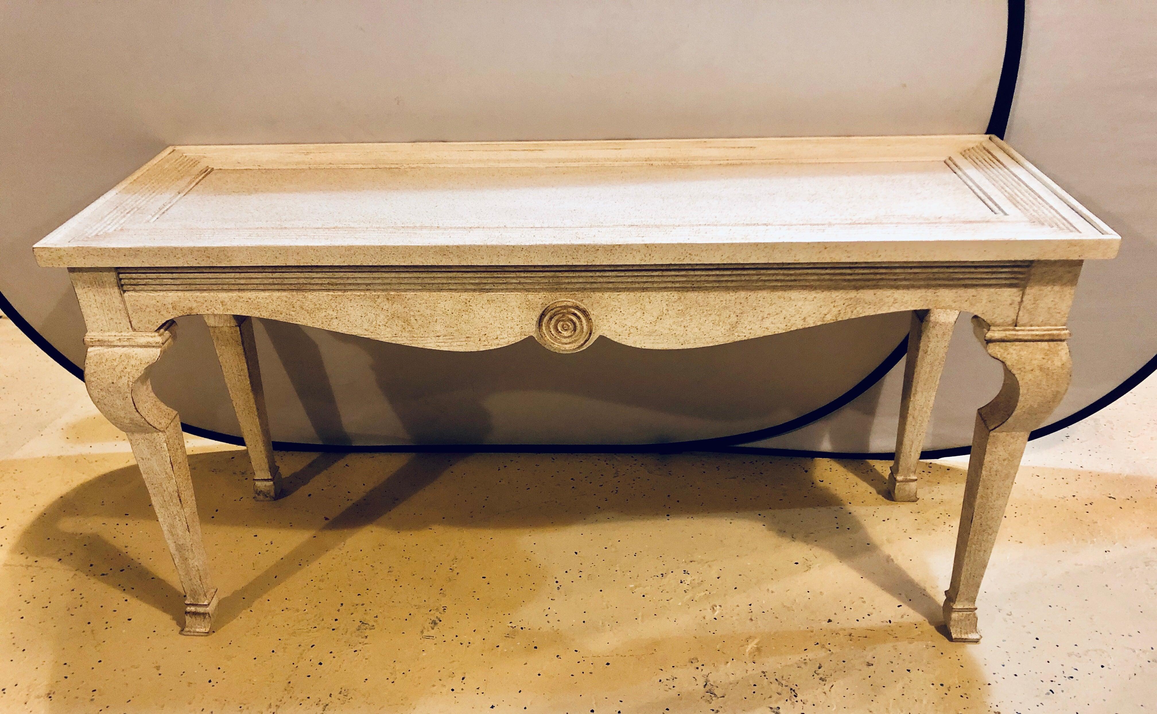 A pair of handcrafted quality Hollywood Regency style center console tables in a pickled off-white distressed finish. Each having the exact same look and design on all sides. This simply stunning pair of console or sofa sideboards are certain to