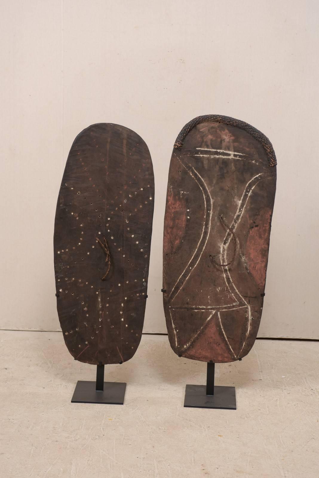 A pair of Papua New Guinea Mendi wooden war shields on custom stands from the mid-20th century. This pair of war shields originate from the Mendi region, within the Southern Highlands of Papua New Guinea. These oceanic war shields were not only