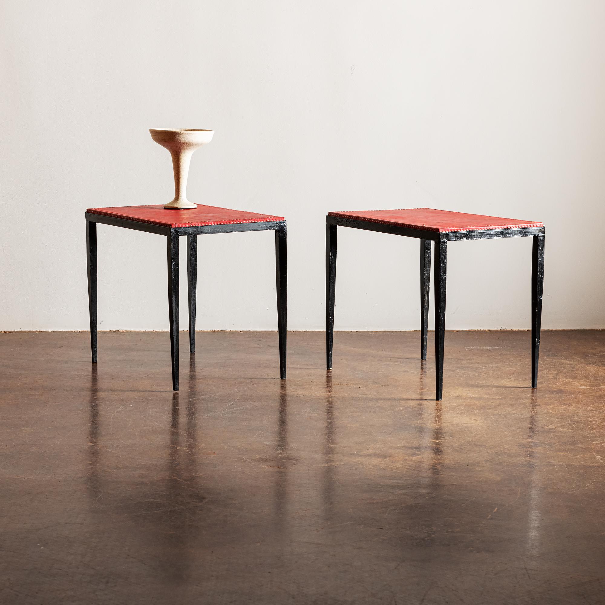 A pair of iron and red leather end tables with contrasting stitching in the manner of Jean-Michel Frank, France, 1940s.