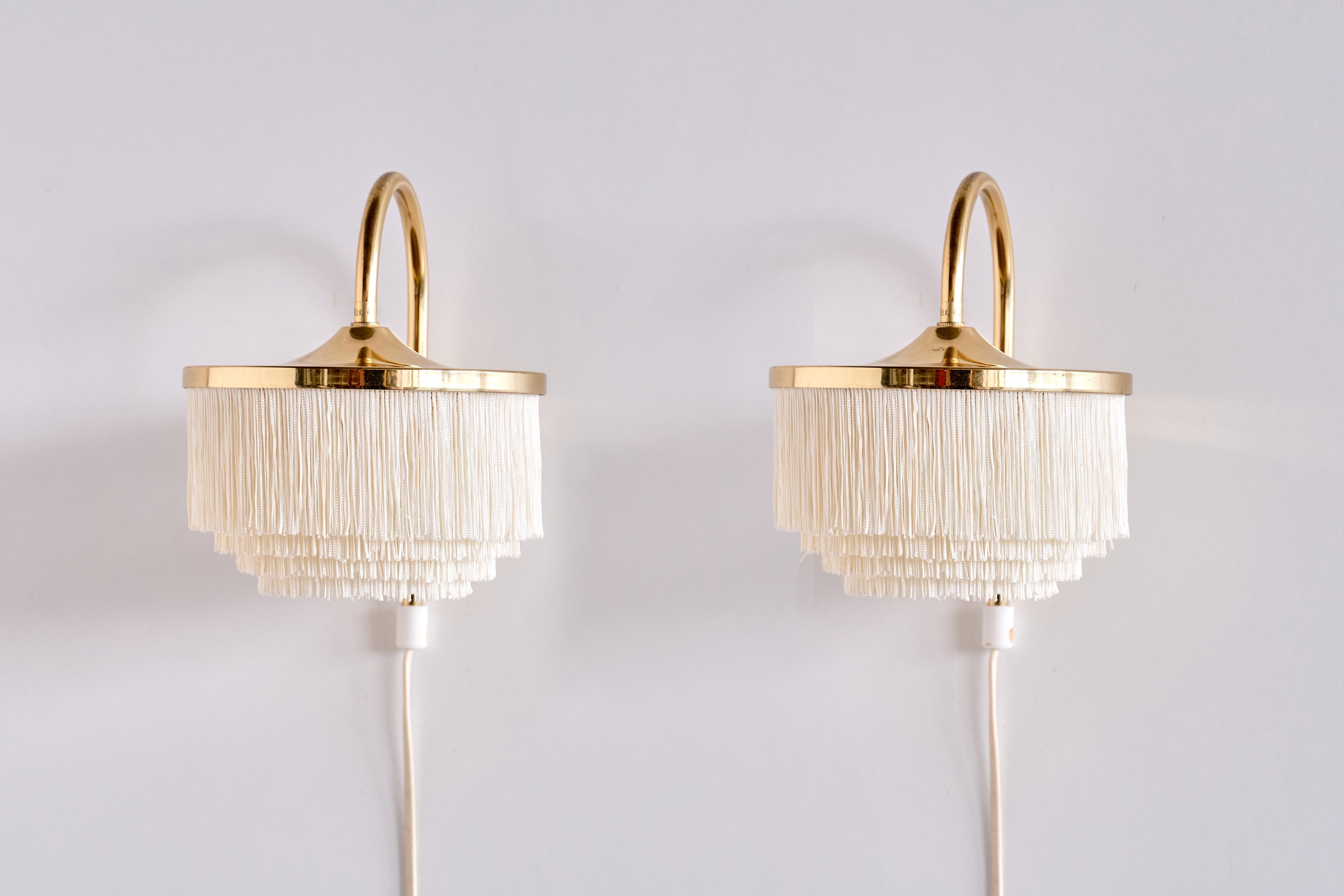 This rare pair of wall lights was designed by Hans-Agne Jakobsson and produced by his company in Markaryd, Sweden in the 1960s. The model is numbered V-271. The lamp consists of a circular brass fixture with four layers of white fringes. Both lamps