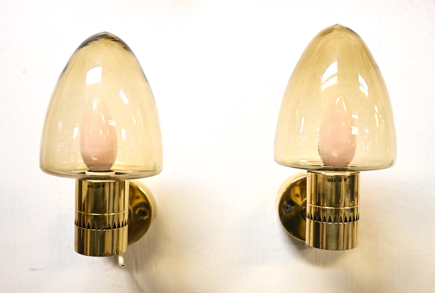 Hans-Agne Jakobsson was a major figure in mid-century Swedish lighting. With a wonderfully elegant design, this pair of sconces casts a warm light, diffused by the mushroom-shaped amber glass shades. These sconces retain the AB Markaryd/Jakobsson