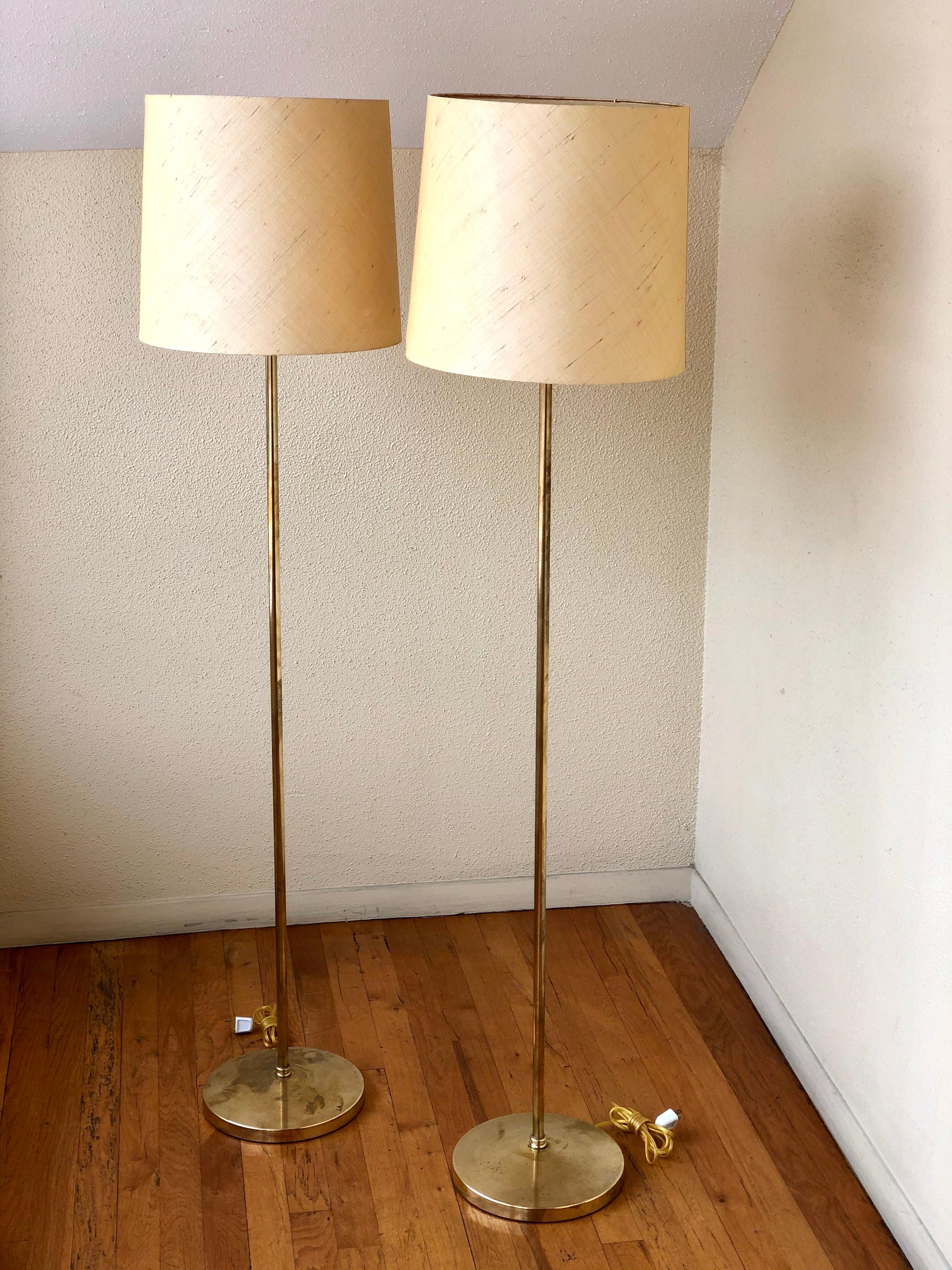 Una coppia molto rara e difficile da trovare di lampade da terra in ottone lucido, circa anni '50. Le lampade sono state ricablate e hanno i loro paralumi originali. Un paralume presenta un danno sul lato, come mostrato, ma è il paralume originale,