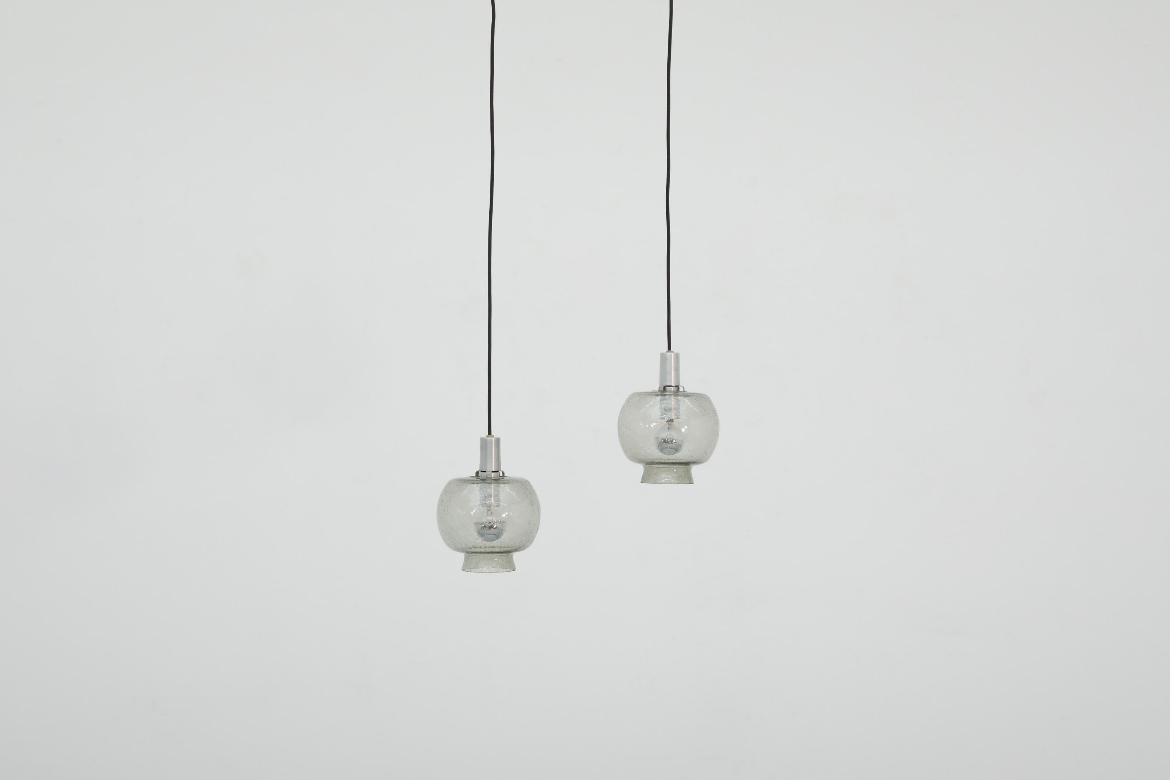 Pair of Hans-Agne Jakobsson style smoked glass pendants with aluminum hardware. Beautiful blown glass shade with embedded bubbles on black cord with metal accents. In original condition with wear consistent with age and use. Set price.