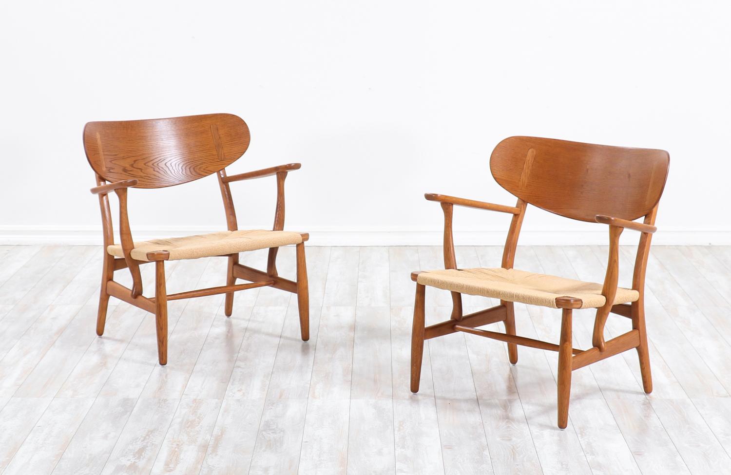 A pair of iconic CH-22 lounge chairs designed by Hans J. Wegner in collaboration with the famous workshop of Carl Hansen & Søn in Denmark during the 1950s. Our chairs feature large molded curbed backrests for optimum comfort that feel as if they hug