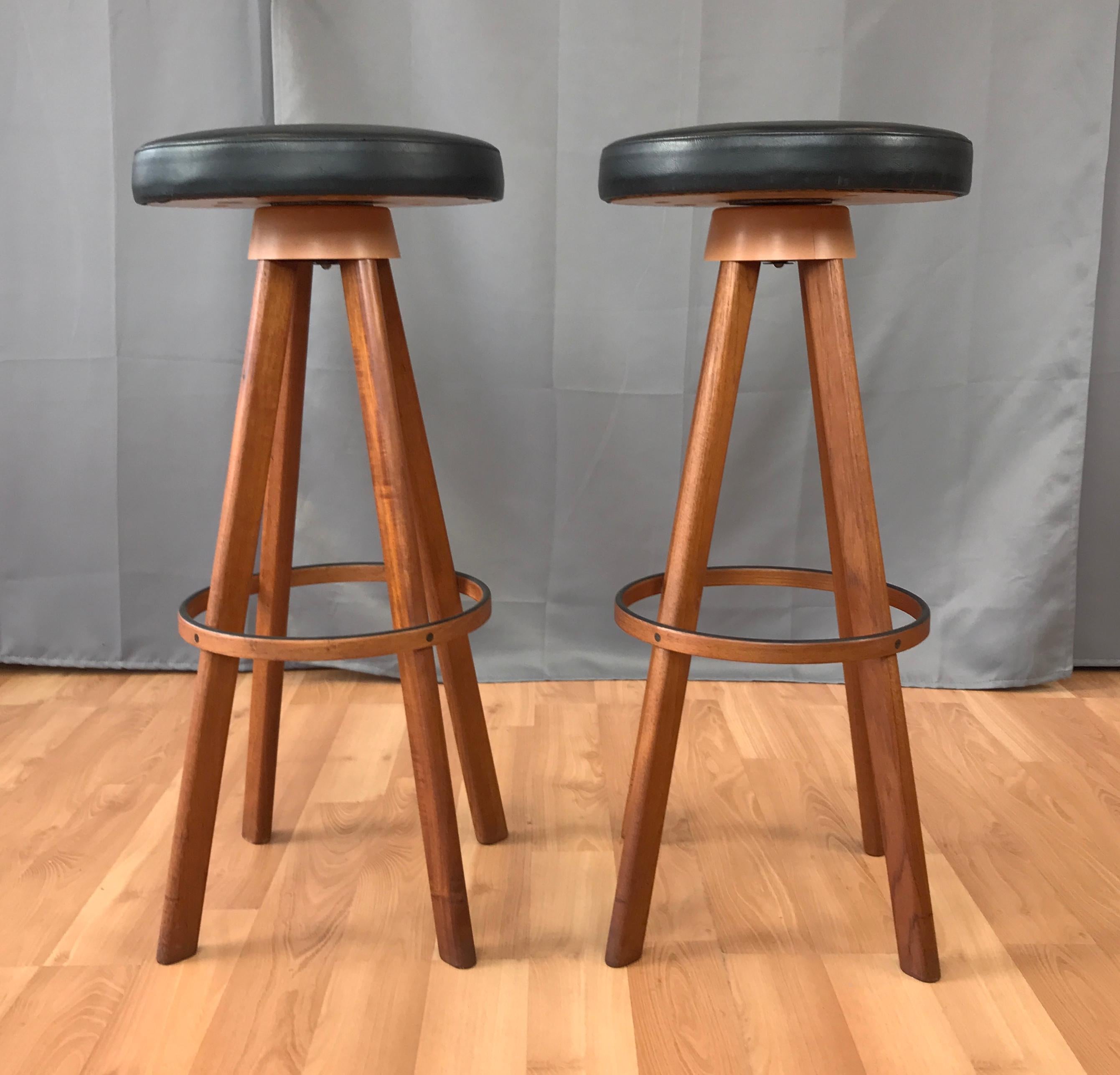 A pair bars stools, designed by Hans Olsen, for Frem Rojle. Solid Teak legs, bent plywood with Teak over footrest, tapers up to a swivelling round black vinyl seats. Marked on their undersides.