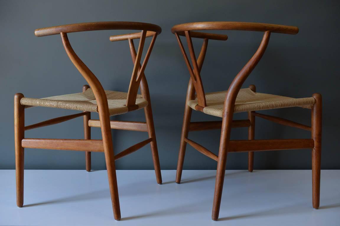 Pair of Hans Wegner CH 24 Wishbone chairs in oak, circa 1960. Original hand oiled oak frames with new papercord seats in excellent condition. Wonderful patina to the oak. Frames are solid. 
Measures H 28.5 in. x W 21.5 in. x D 20 in.