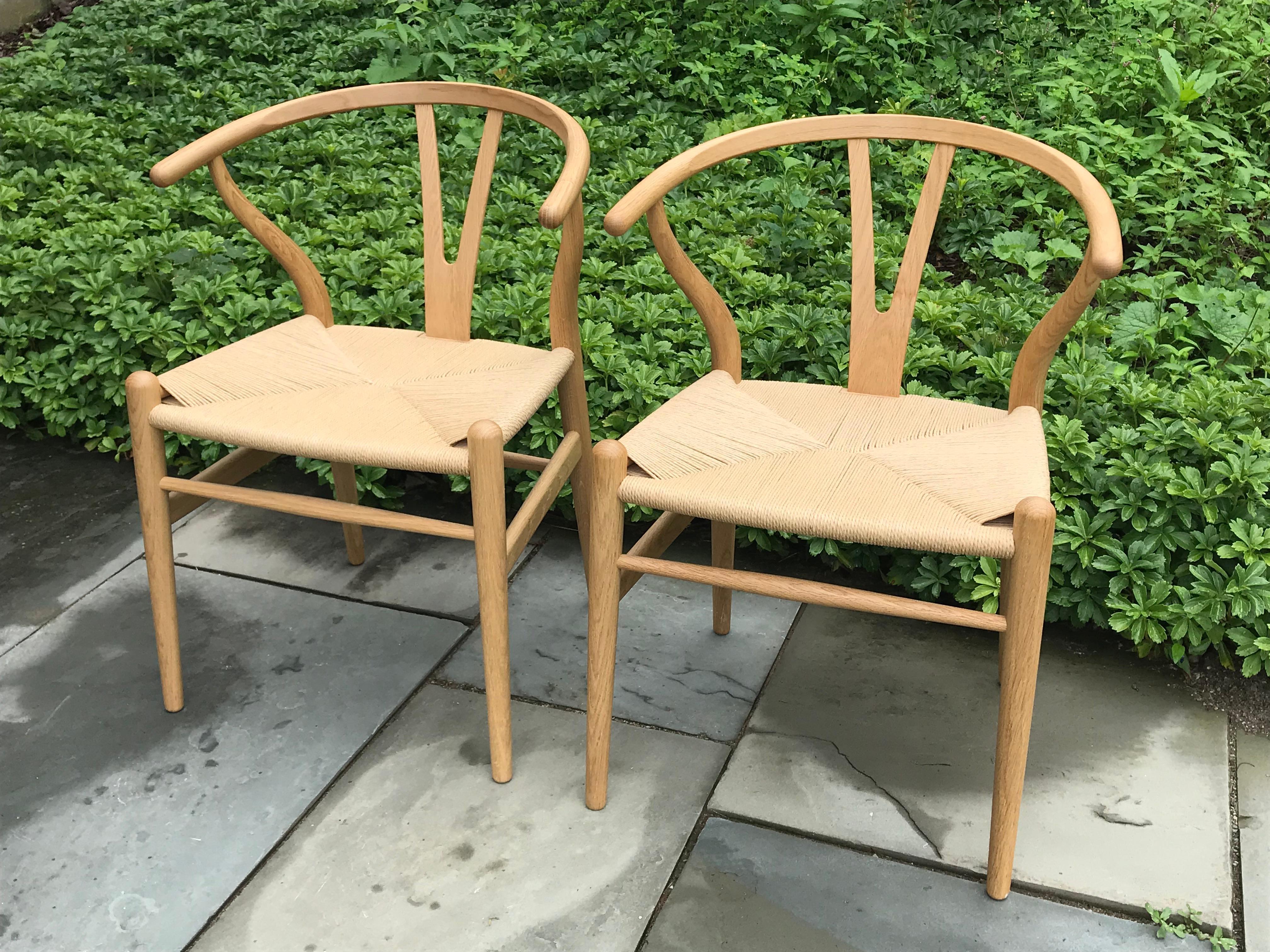 Pair of recent production Hans Wegner wishbone chairs in bentwood oak with handwoven seats.

In 1944, Danish designer Hans Wegner began a series of chairs that were inspired by portraits of Danish merchants sitting in Ming chairs. One of these