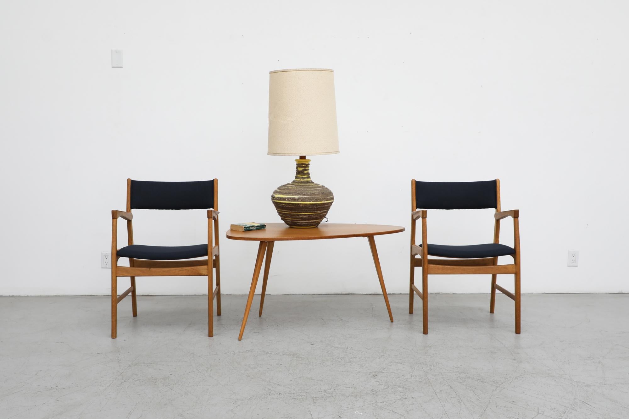 Pair of midcentury Danish oak armchairs in the style of Hans Wegner. These chairs have solid oak frames, delicately carved armrests and newly upholstered black fabric seating. The frames are in good original condition with wear consistent with their