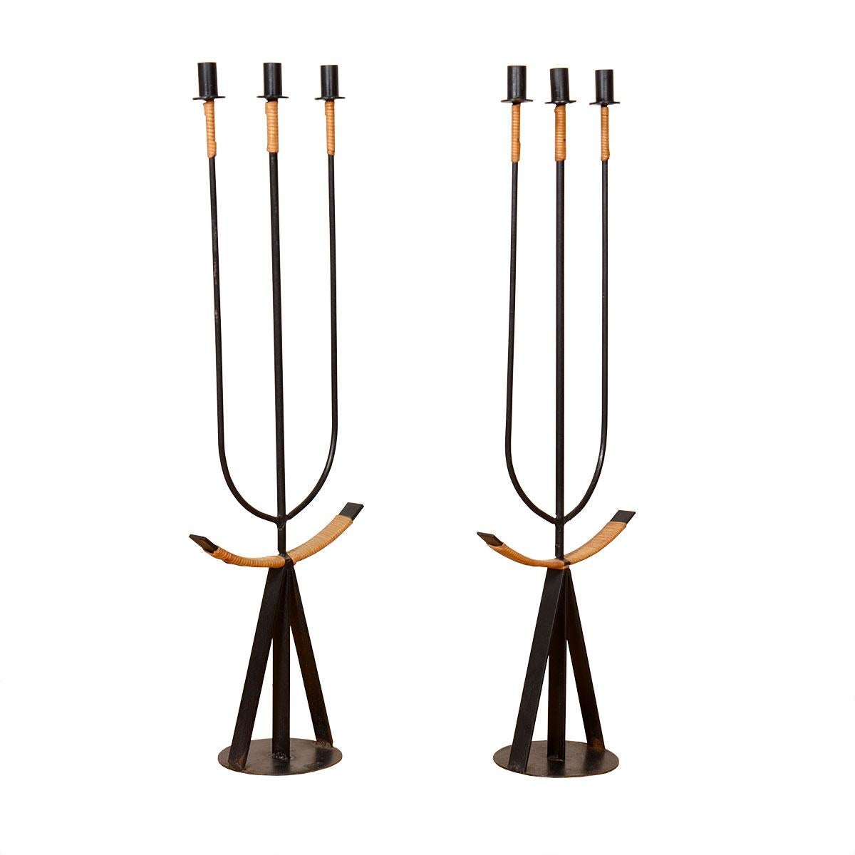 Pair of Wrought Iron candelabra with rattan detailing. Iconic design by Arthur Umanoff from the 1950s. 3 tall, elongated stems have a wrapping of rattan at the neck just below the candleholder. 3 stem base on a circular foundation with “arms”