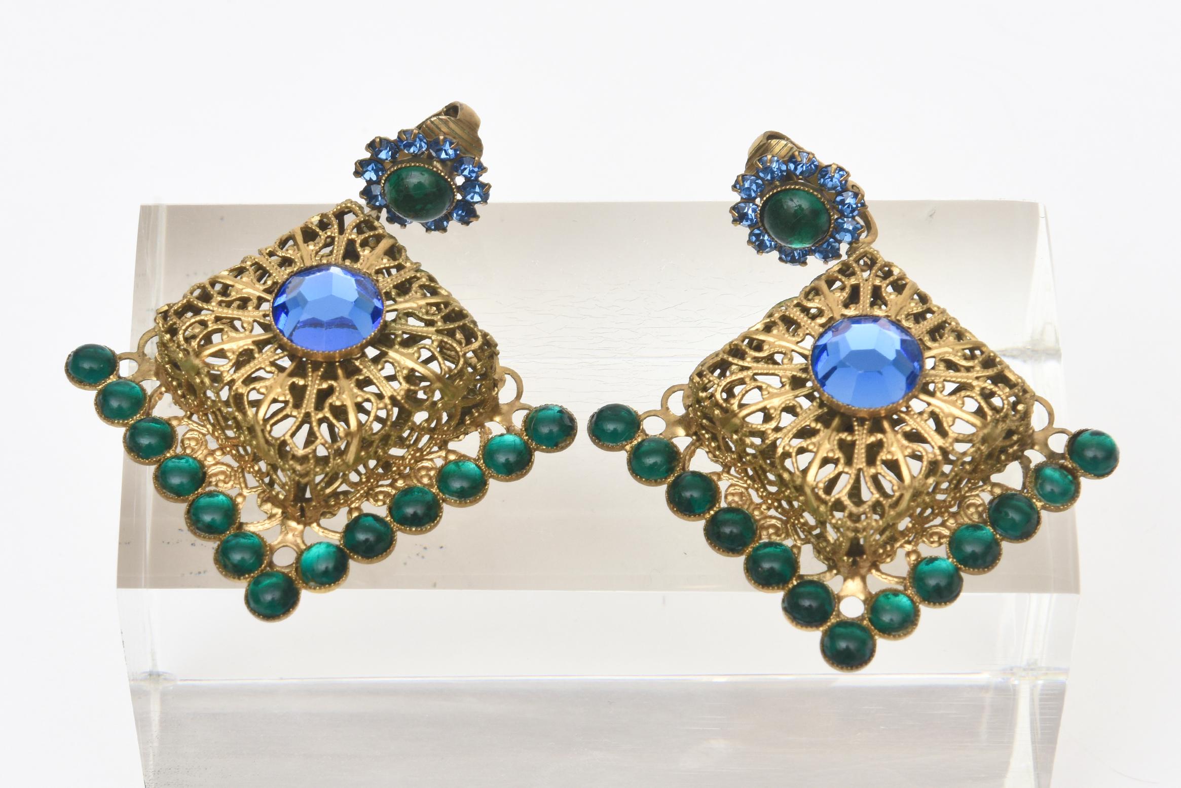 These pair of amazing and dramatic vintage signed obscure early Hattie Carnegie clip on multi colored jewel toned dangle chandelier earrings are an eye catcher on the ear lobes. Greens and blues join together against beautiful gold gilt filigree