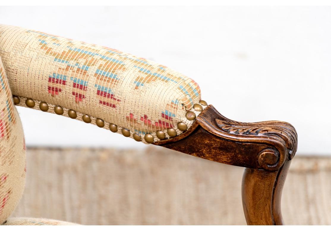 Pair of Provincial French style lounge chairs upholstered in a textured woven tan fabric with colorful abstractions. The chairs with stylized wings, manchettes, brass tacks, serpentine front and resting on carved cabriole legs.

Dimensions: 27