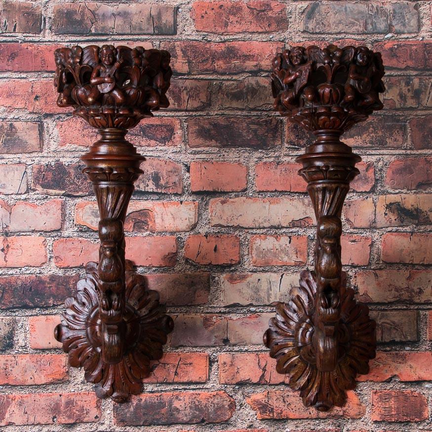 Exceptional well carved pair of candle wall sconces from Sweden. Note the hint of gold paint over the dark red / burgundy base color that enhances the hand carved details and rich patina. Each sconce is carved with five cherubs playing musical
